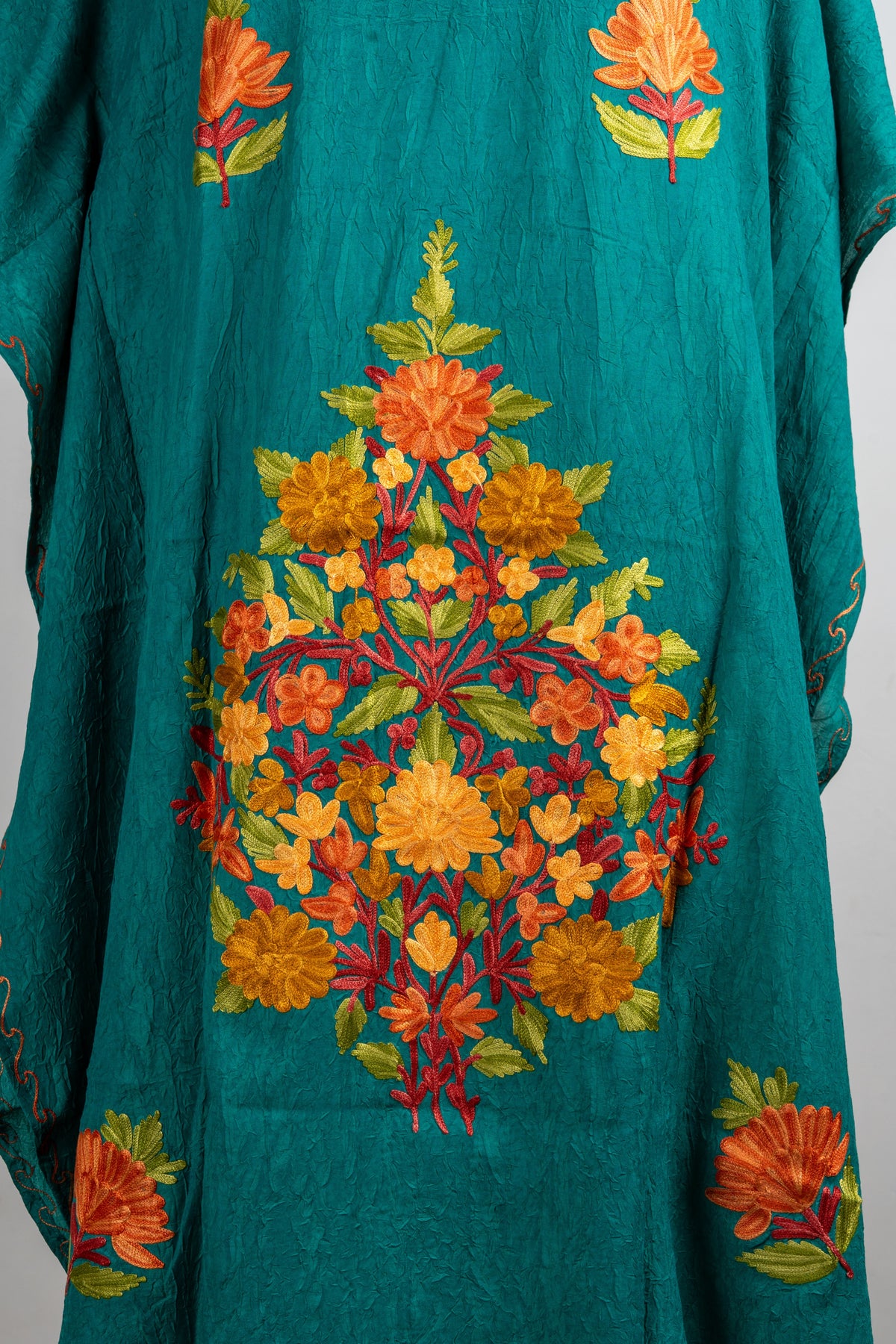 Close-up of the kaftan central bouquet with orange and yellow flowers, green leaves and red branching stems on teal.