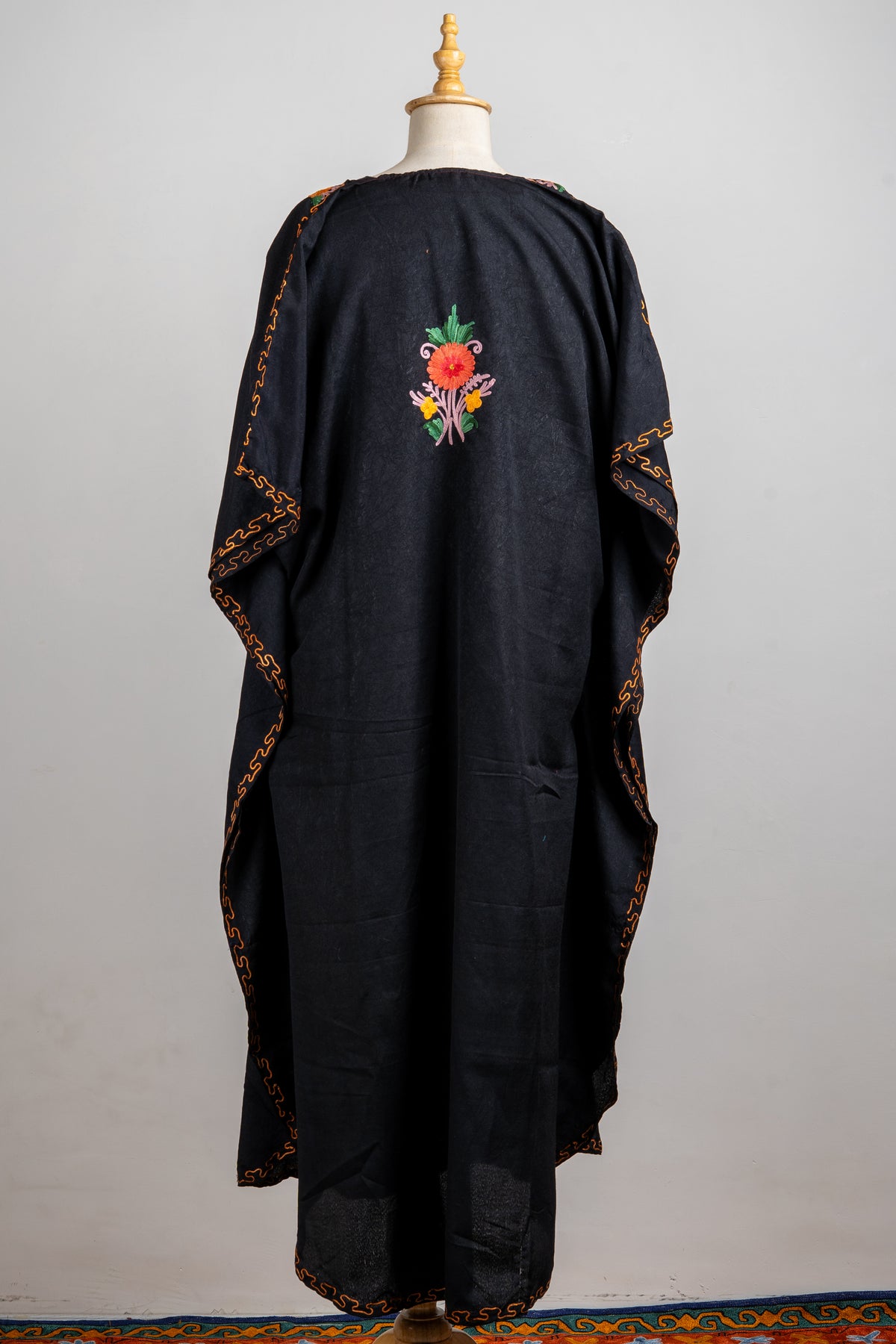 Back of a black kaftan with one small Aari floral spray high in the centre and narrow golden embroidery around the edges