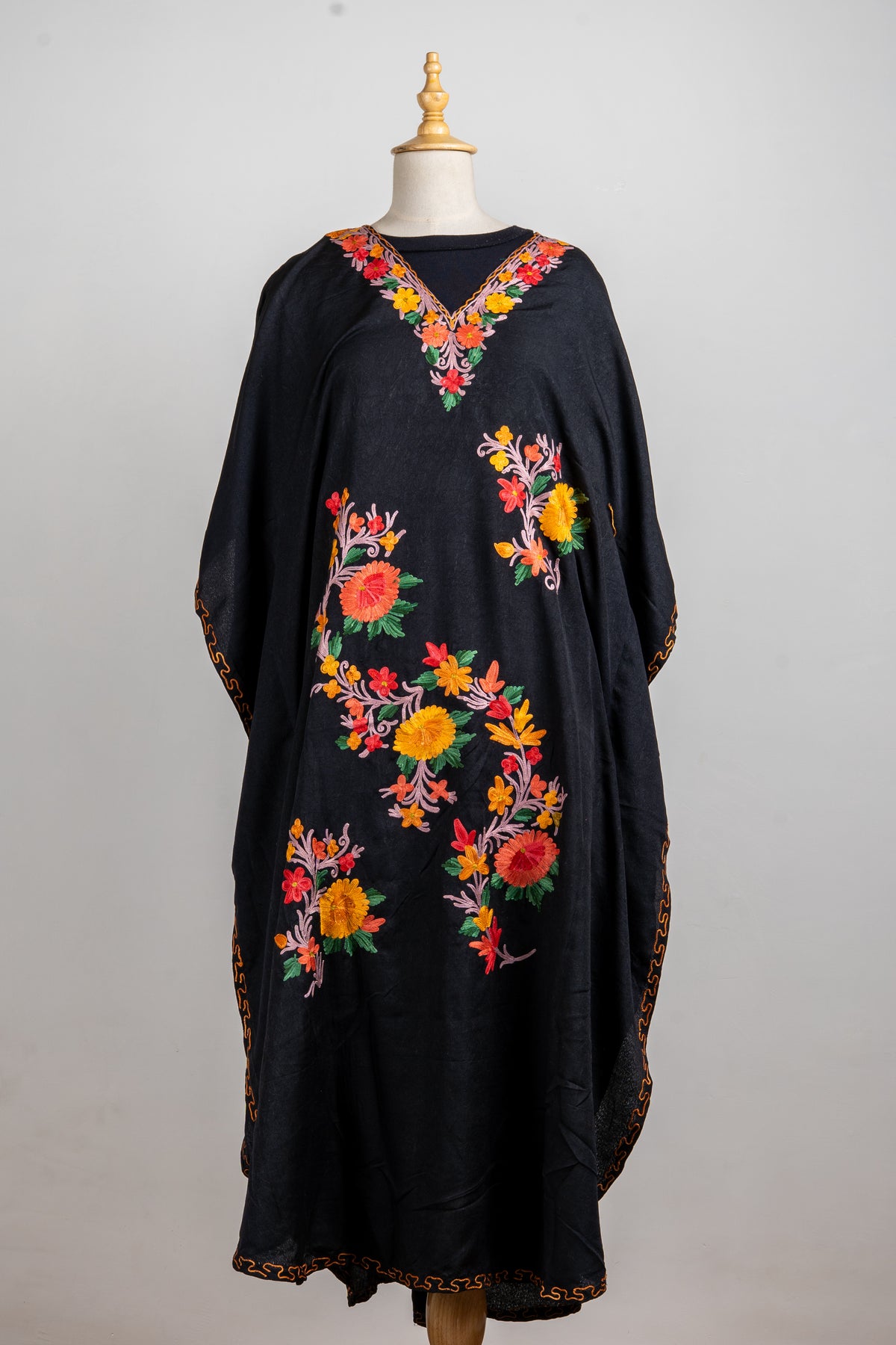 Full front of a flowing black kaftan with bright Aari flower sprays, an embroidered V-neck and golden hem edging
