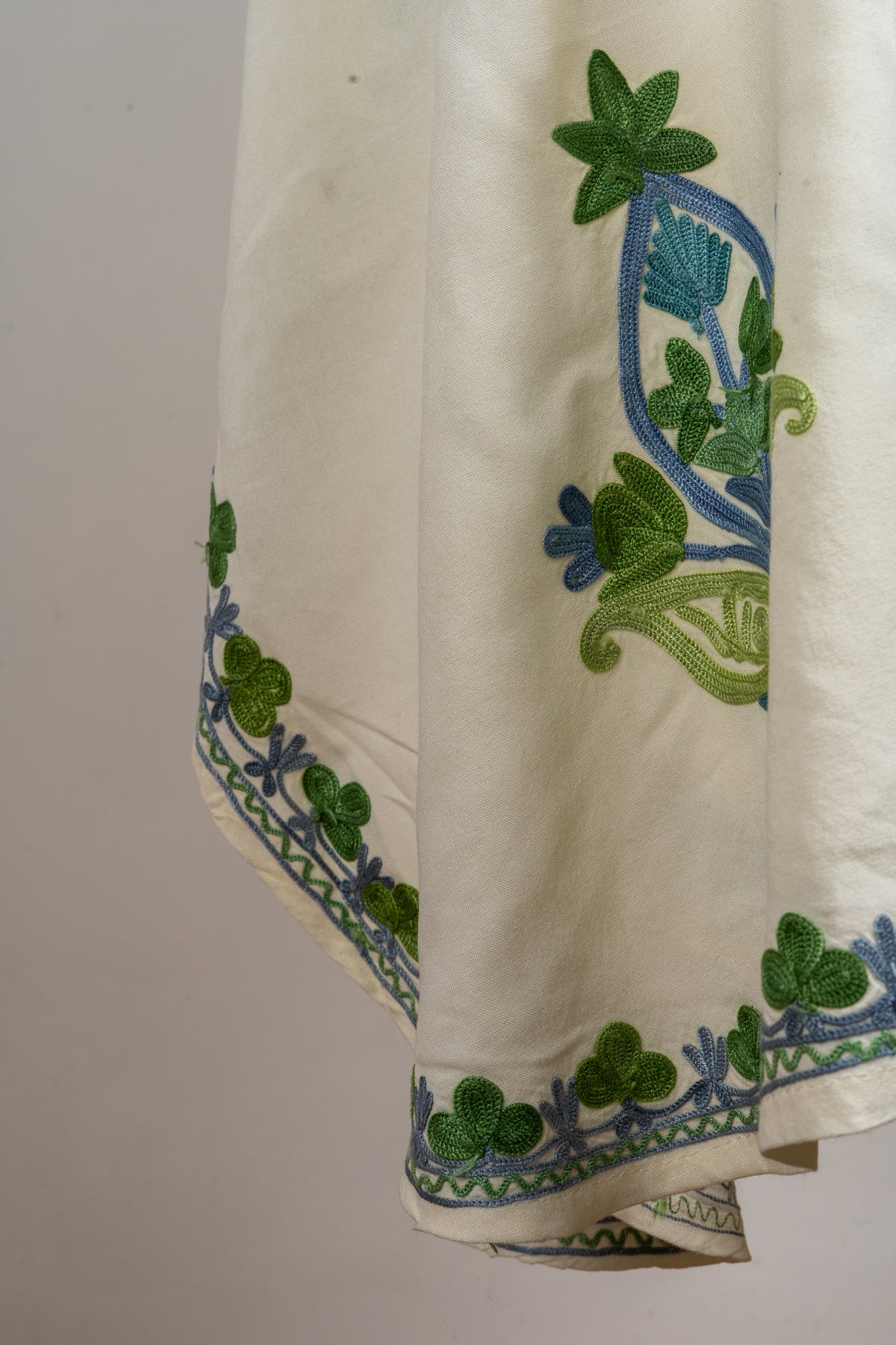 Detail of green and blue floral embroidery along the ivory kaftan’s hem and hanging side