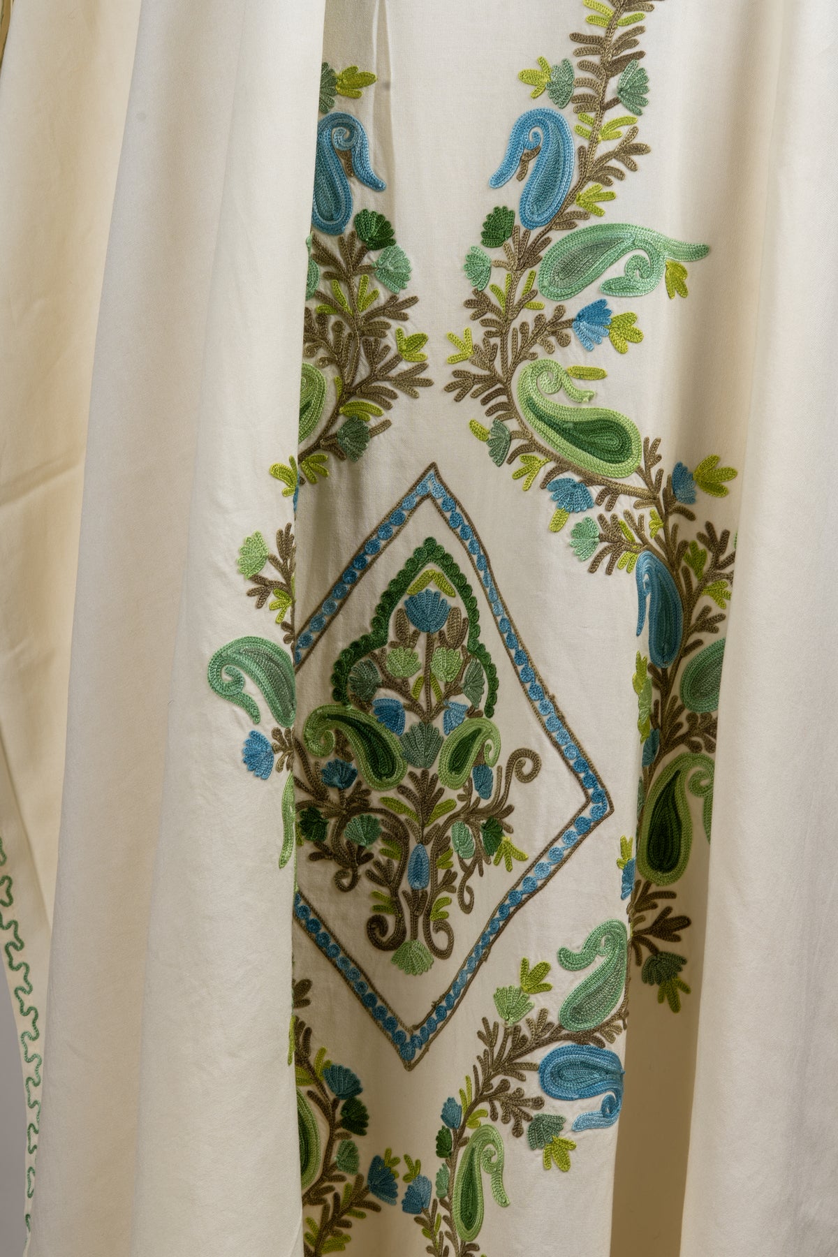 Close-up of the ivory kaftan’s central diamond motif, filled with green leaves, blue paisleys and brown stems