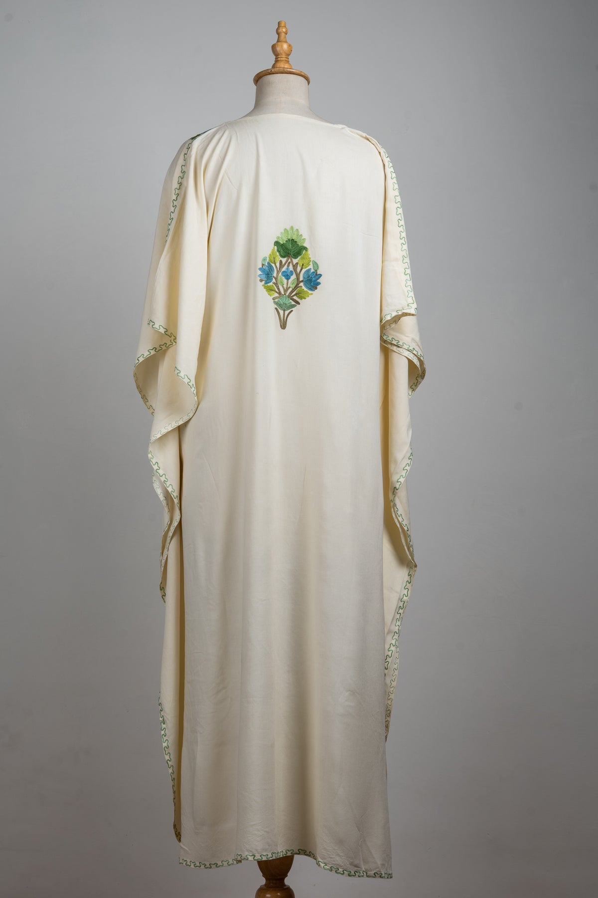 Full back view of the ivory kaftan, with a small blue-and-green floral motif and narrow embroidered sleeve edges