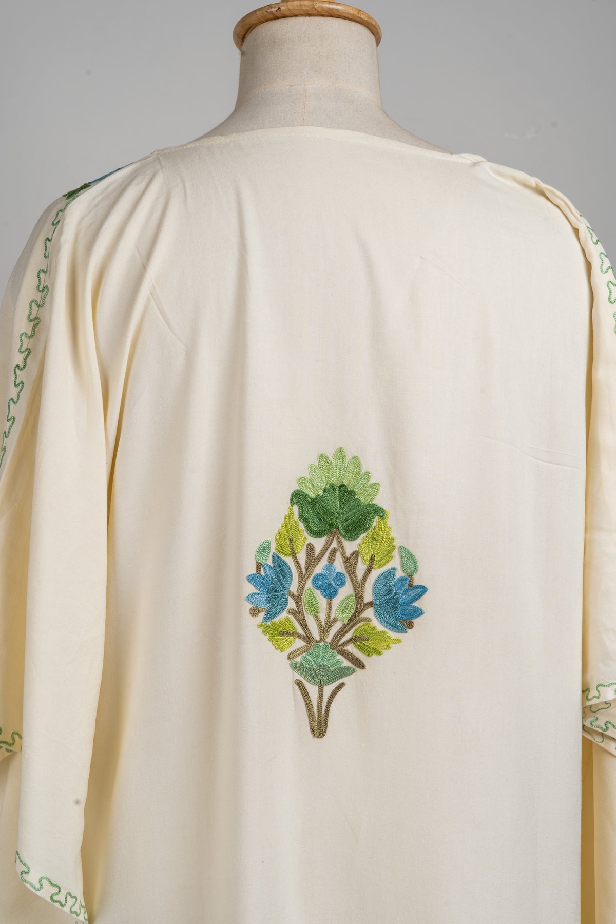 Close-up of a small blue-and-green floral spray between the shoulders on the ivory kaftan’s back