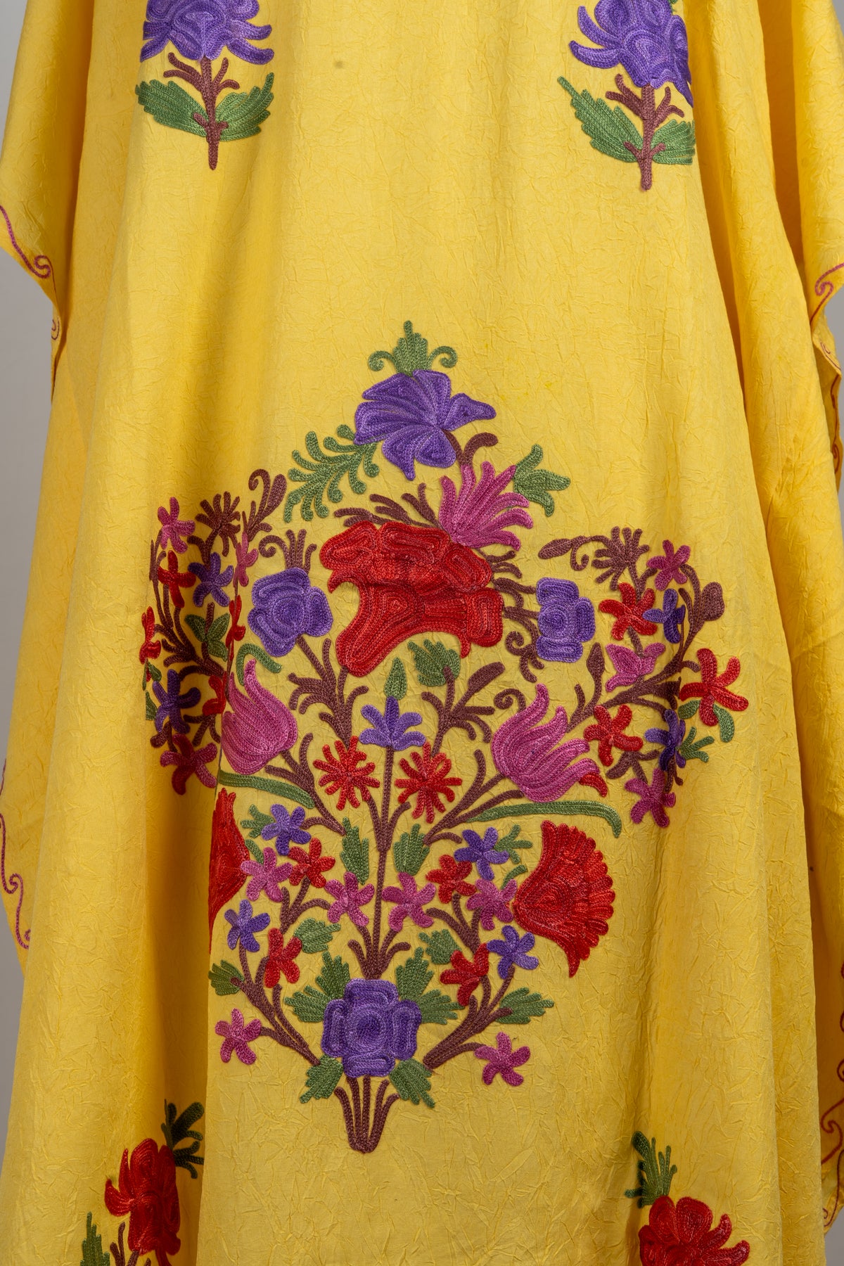 Close-up of a large red and purple Aari floral bouquet with green leaves on a yellow kaftan