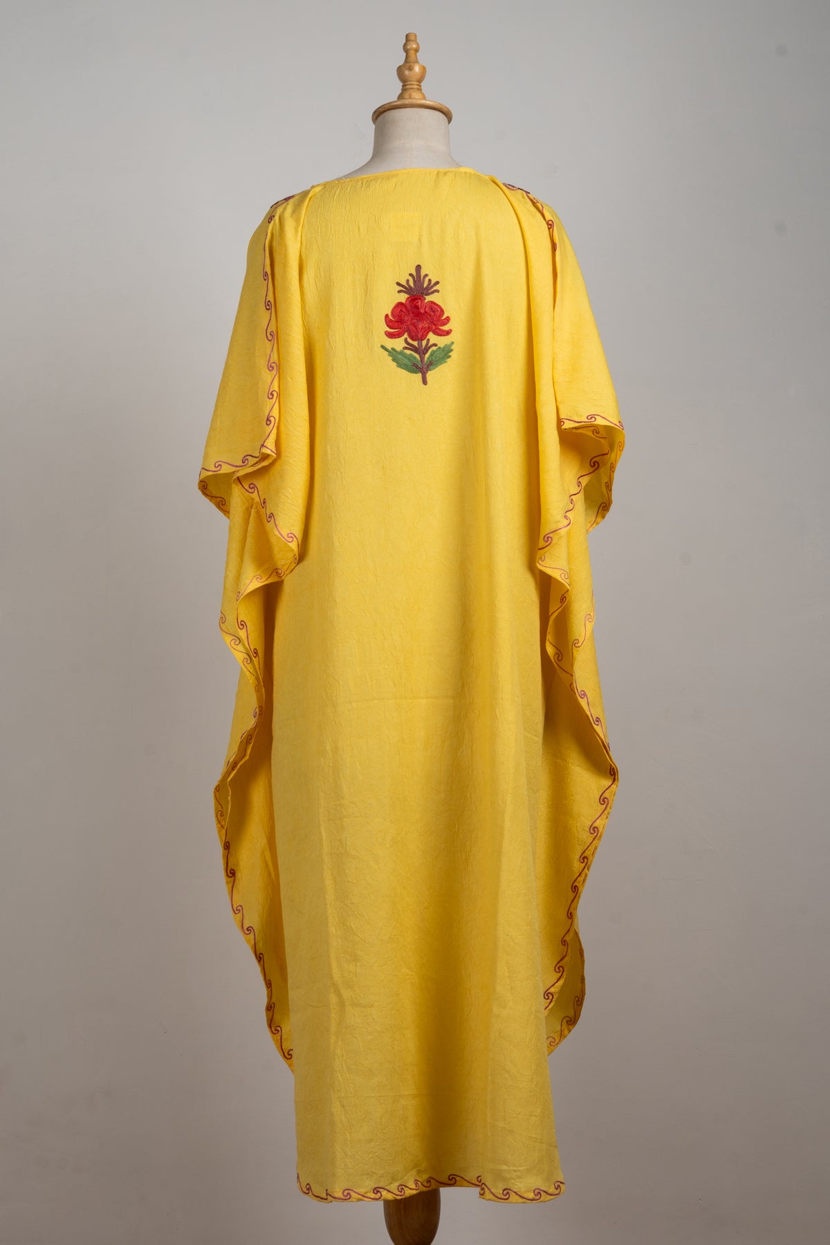 Back of a flowing yellow kaftan with a single red Aari flower high in the centre and fine embroidered edges