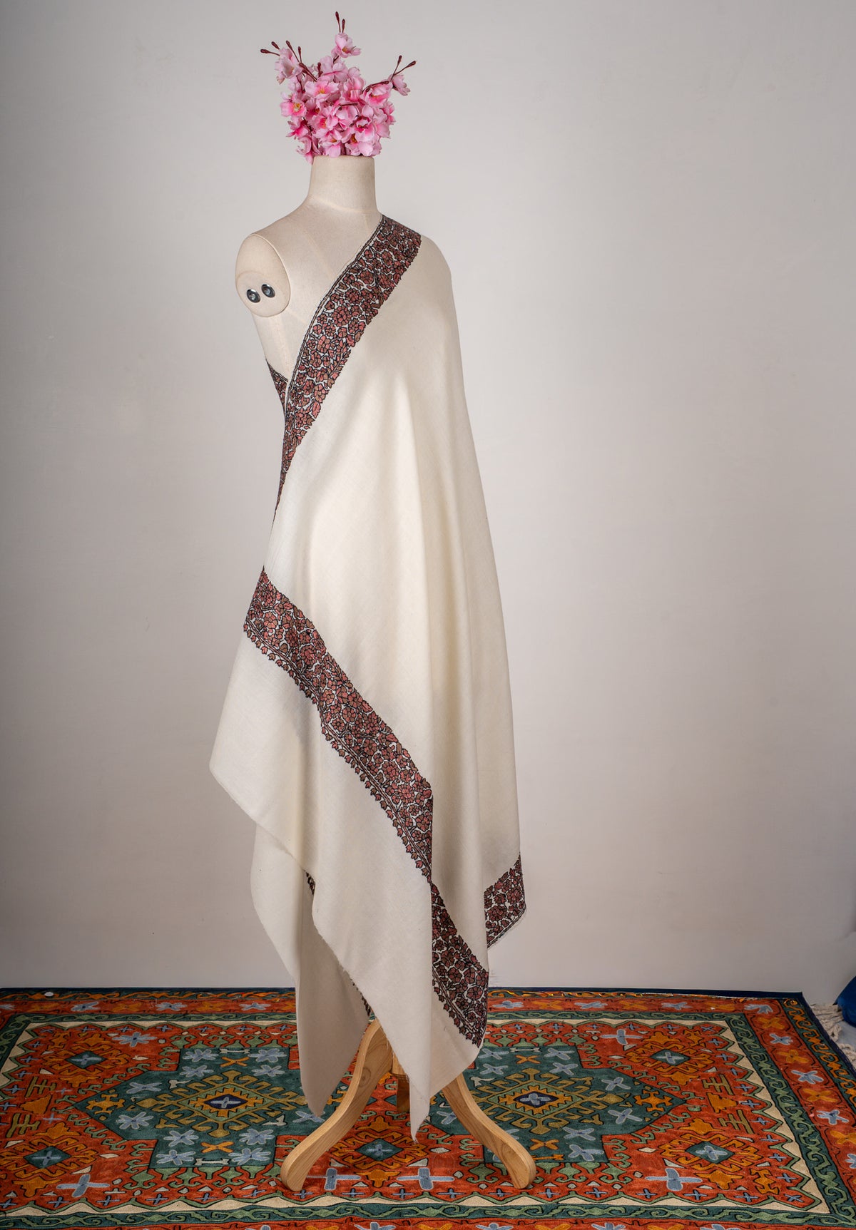 Full view of an ivory Merino wool shawl draped over a mannequin with red and black floral borders