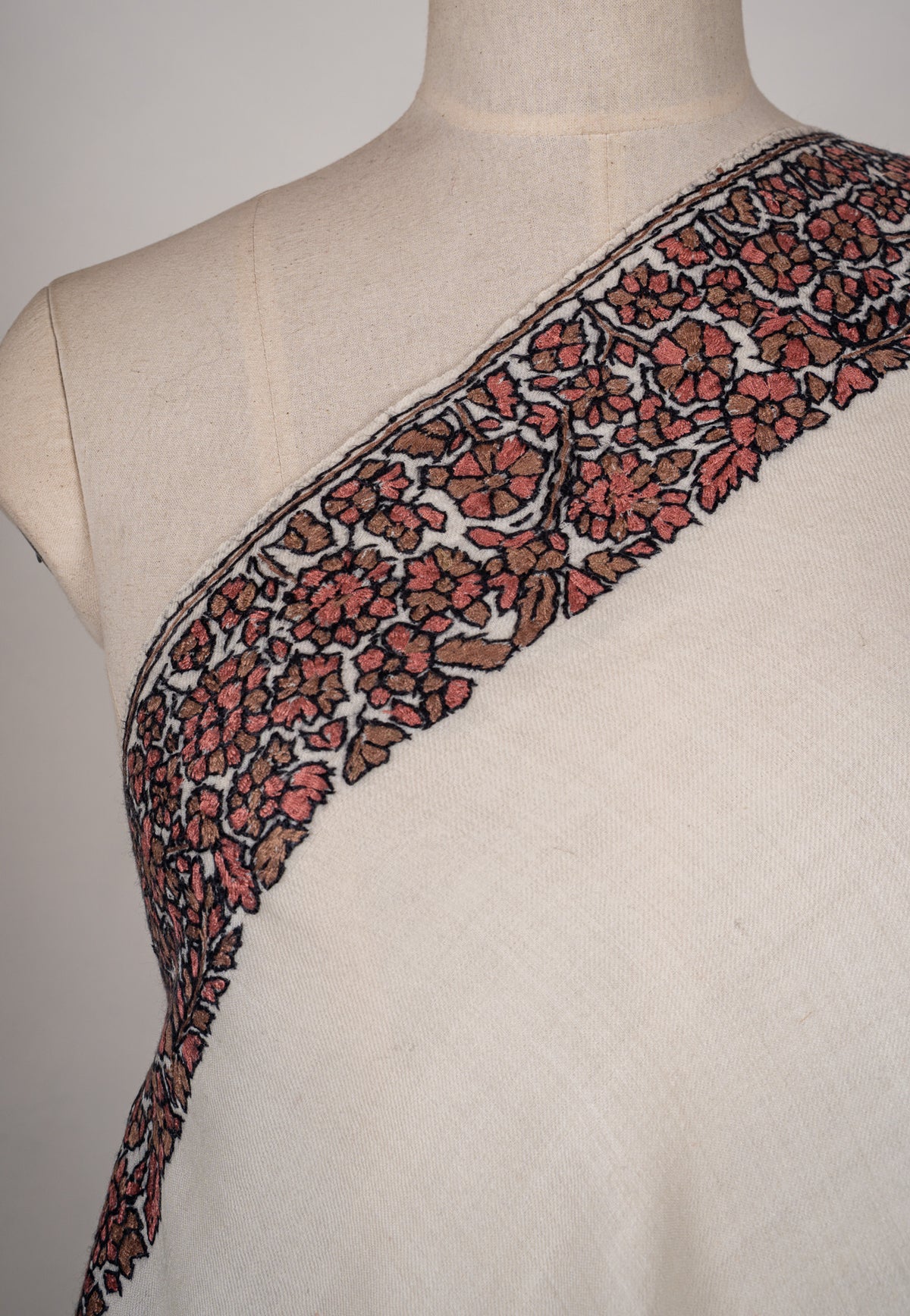 Close-up of muted red Sozni flowers and black-outlined vines across the shoulder of an ivory shawl