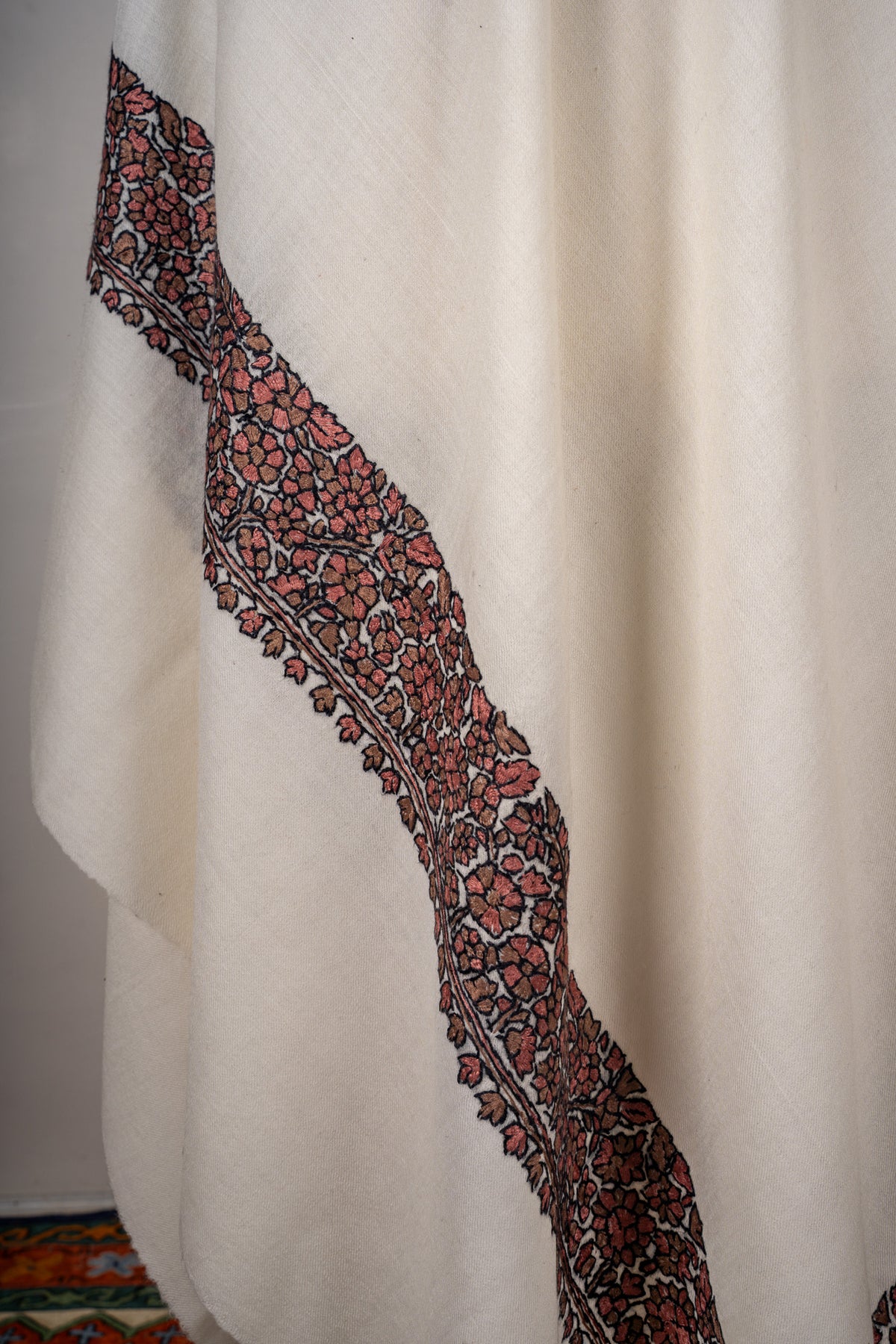 Hanging fold of an ivory shawl showing a muted red floral Sozni border outlined in black