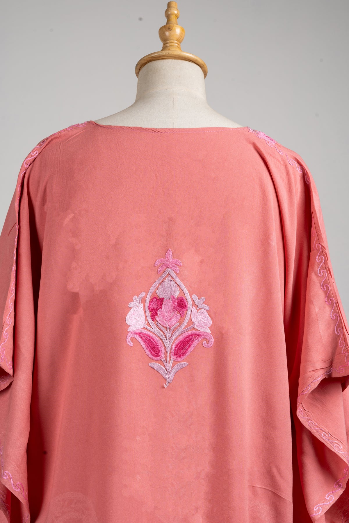 Close-up of the rose-pink kaftan’s back, with a small blush-and-fuchsia flower motif below the neckline