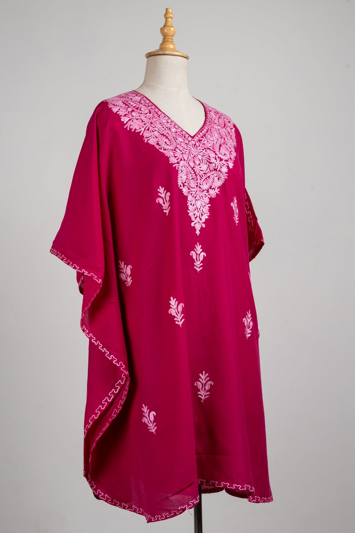 Angled full view of the ruby pink kaftan, with a pale pink embroidered neckline, scattered sprigs and loose sleeves