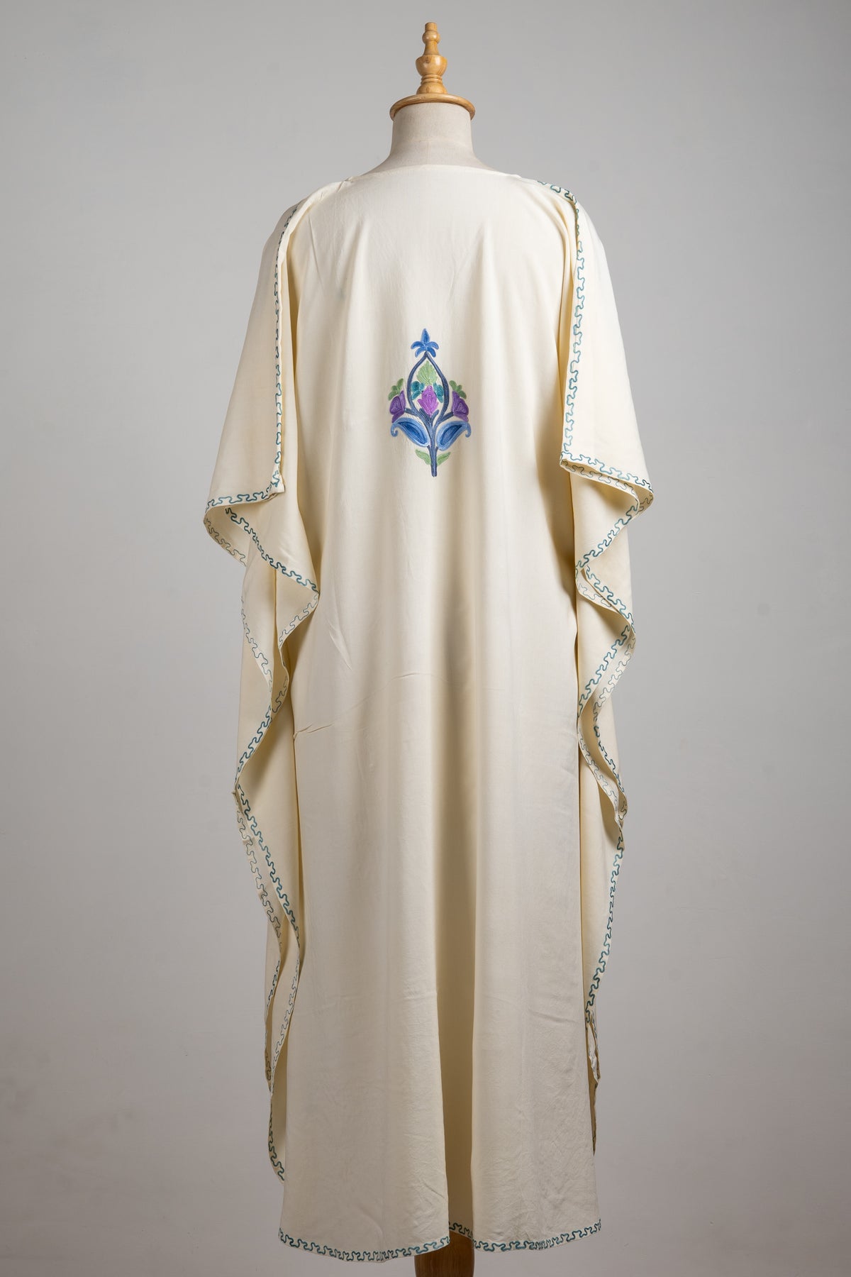 Full back view of the ivory kaftan with a single blue and purple floral motif and fine teal edging around sleeves and hem.