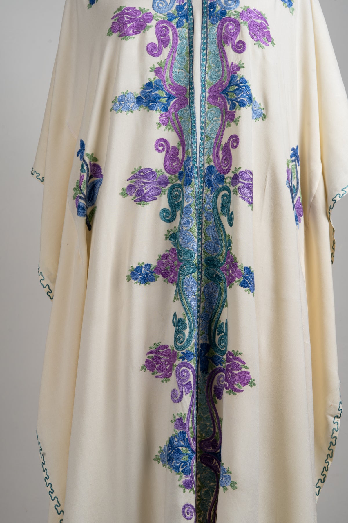 Close-up of the kaftan vertical front embroidery with paired purple paisleys, blue flowers and pale green leaves.