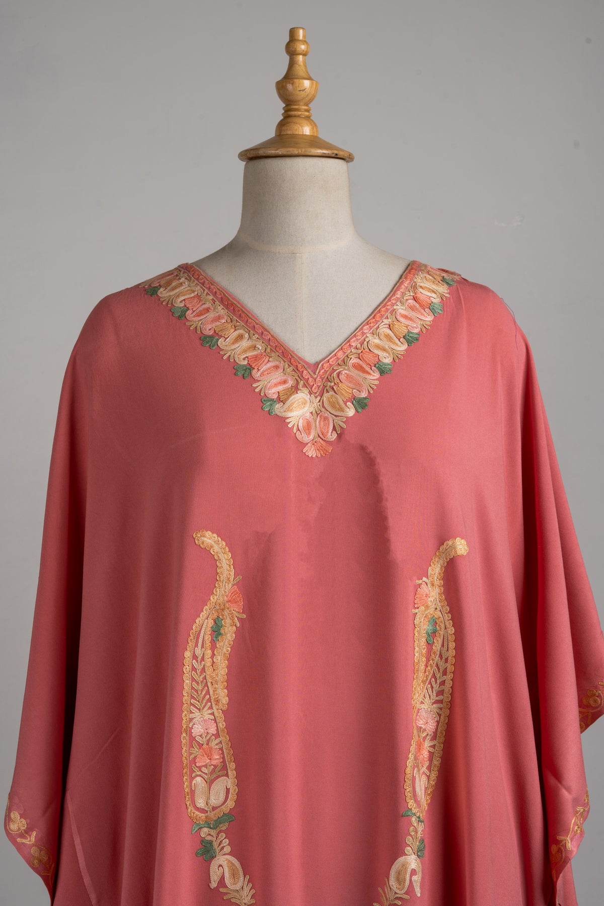 Upper front of a blush-rose kaftan, with champagne floral embroidery around the V-neck and two tall paisleys below