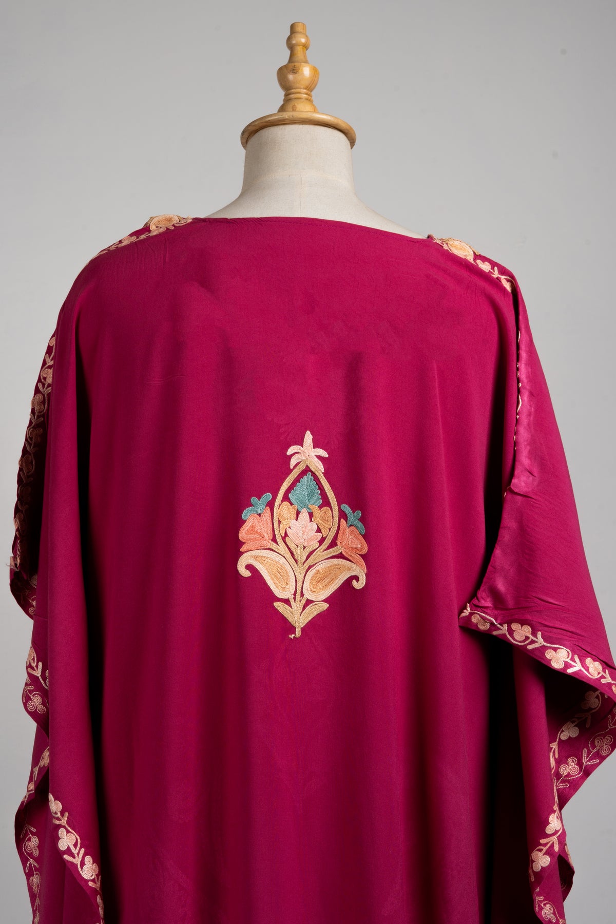 Close view of a single peach, beige and teal embroidered floral motif on the fuchsia kaftan’s back