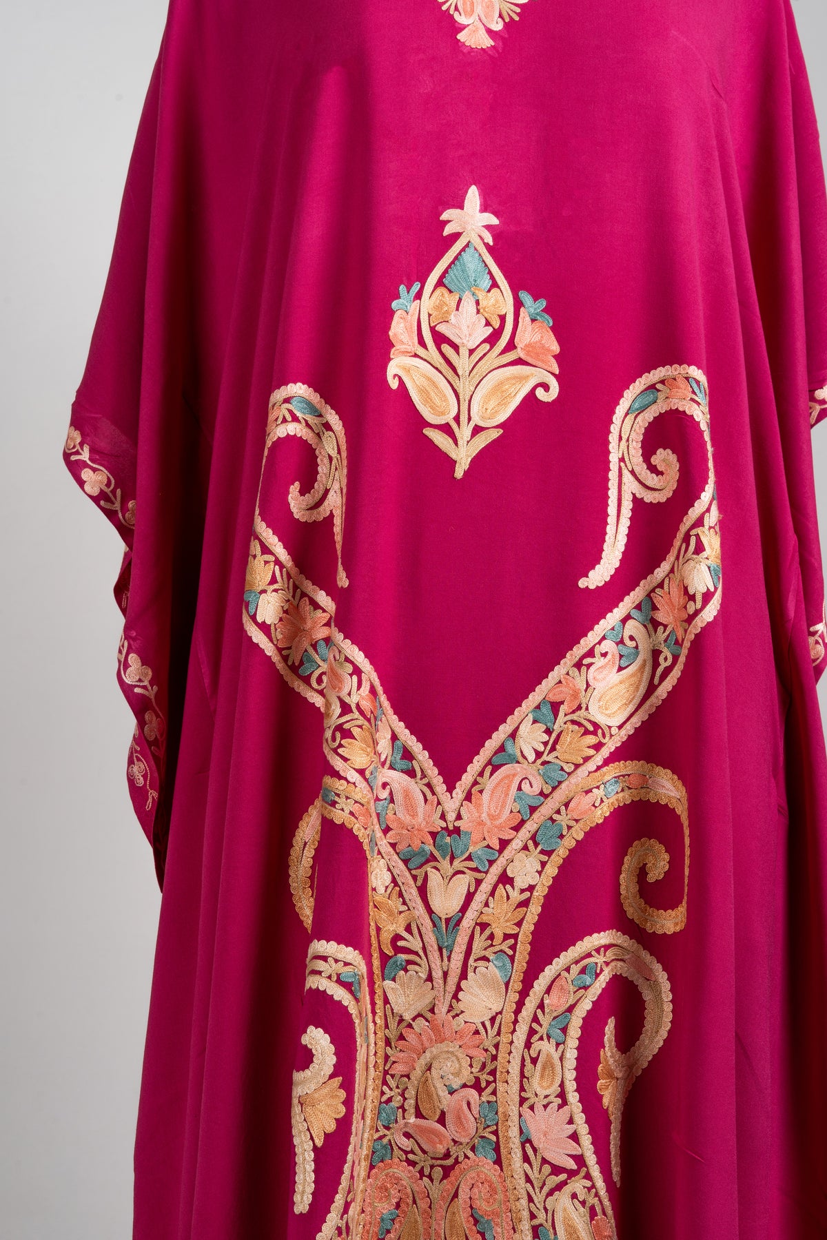 Detail of the fuchsia kaftan’s large symmetrical scrolling motif filled with peach and beige flowers and teal leaves
