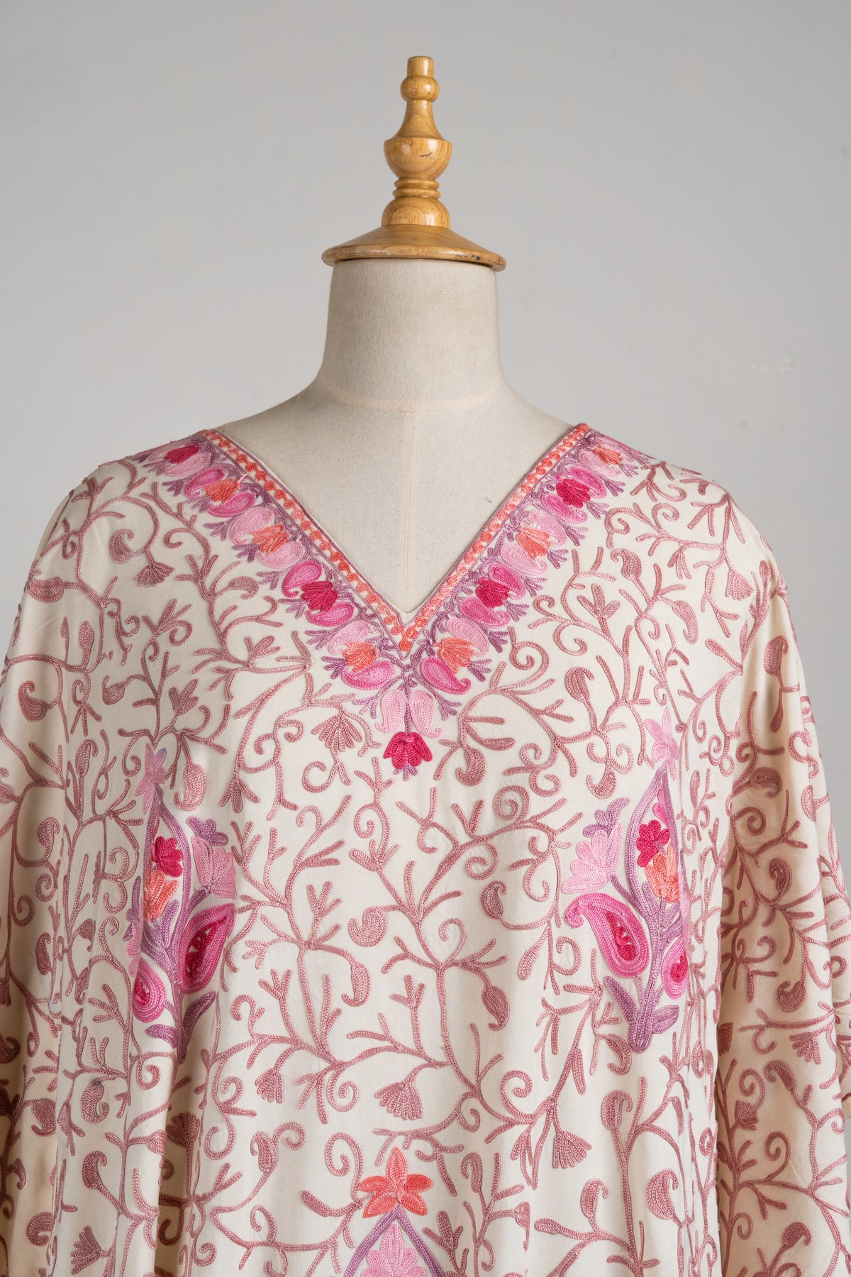 Upper front of a cream kaftan with fine pink Aari vines, larger pink flower motifs and a floral V-neck border