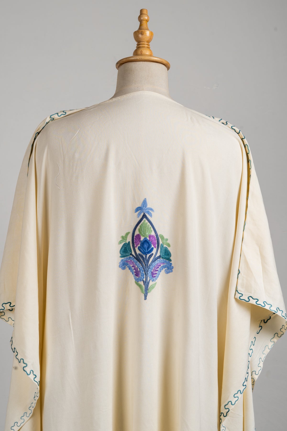 Close-up of a blue, teal and lavender floral motif between the shoulders on the cream kaftan’s back