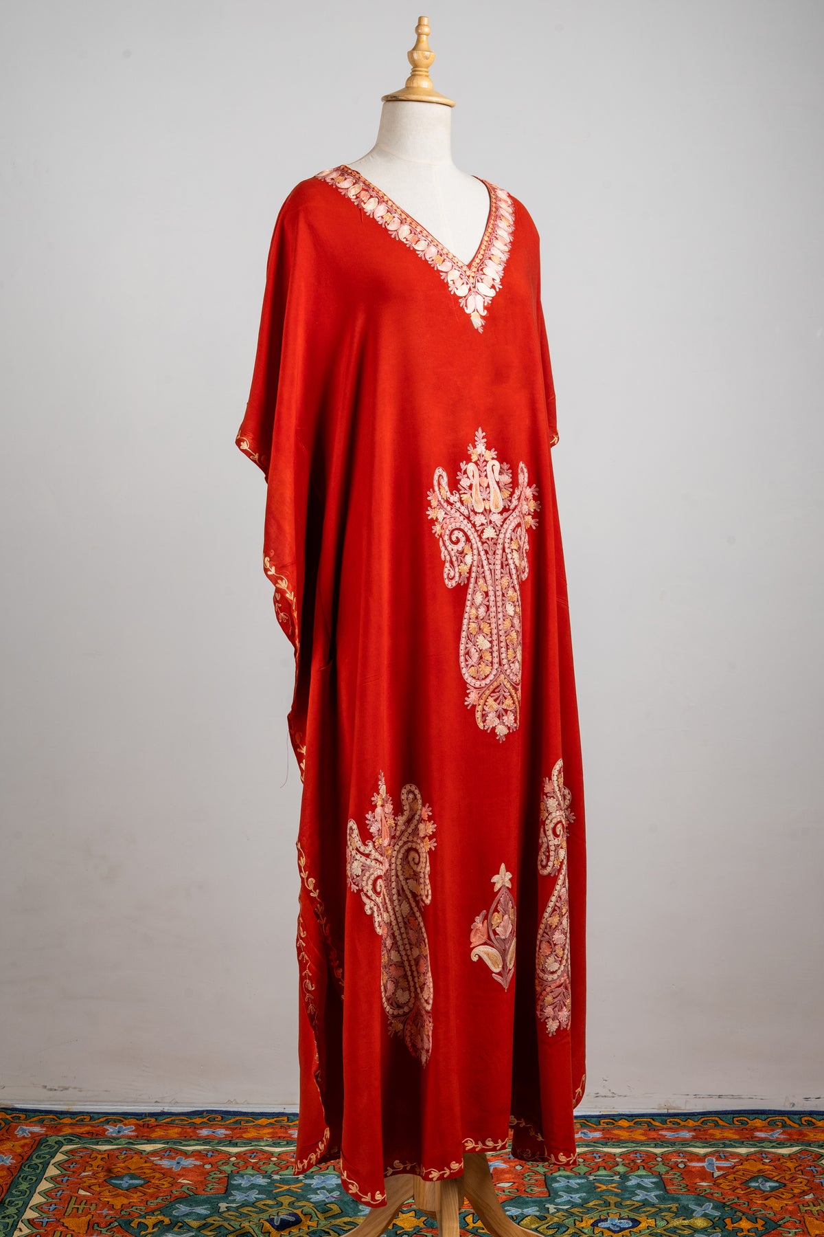 Angled full view of the rust-red kaftan with a pale embroidered neckline, large scrolling medallions and loose sleeves