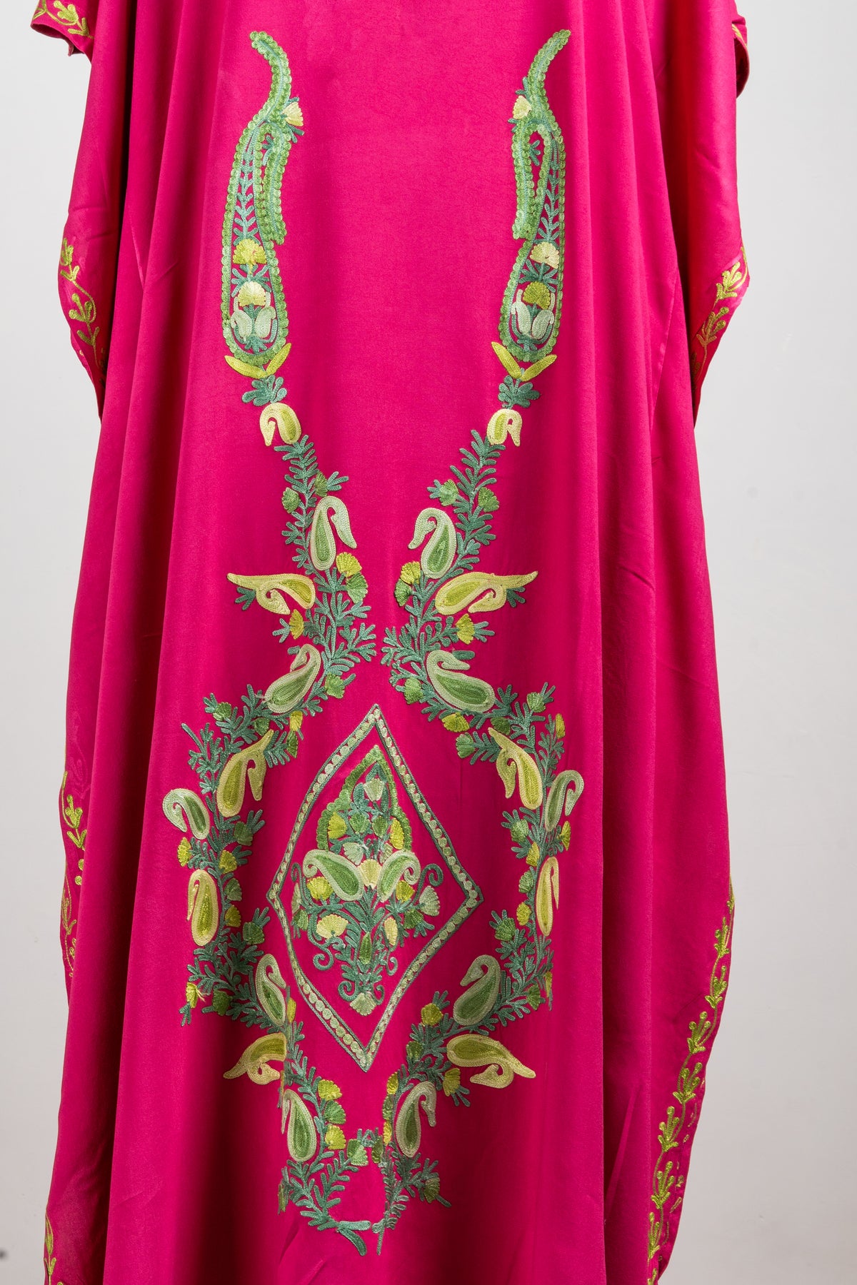 Detail of tall green-and-gold paisleys and a central diamond-shaped floral design on the fuchsia kaftan’s front