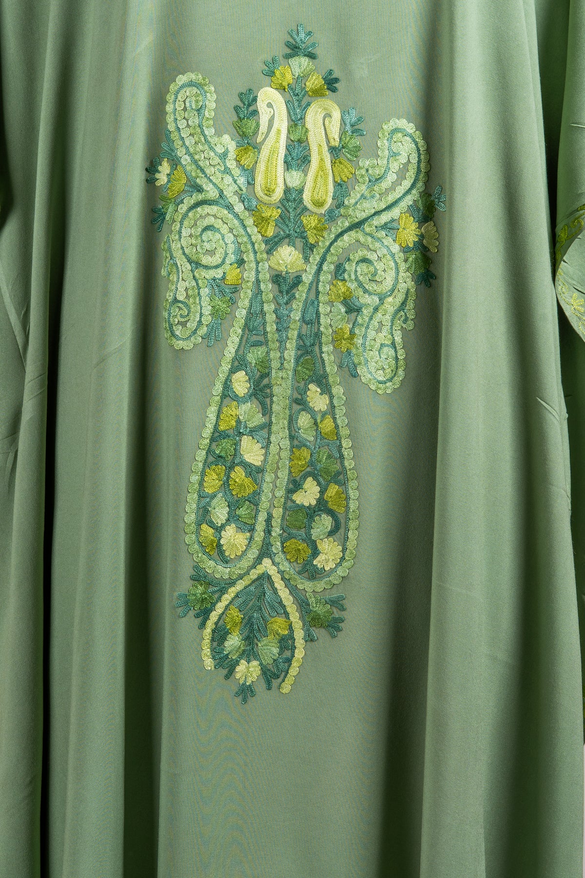 Close-up of a long symmetrical Aari paisley motif with pale lime outlines, green leaves and small flowers on green fabric