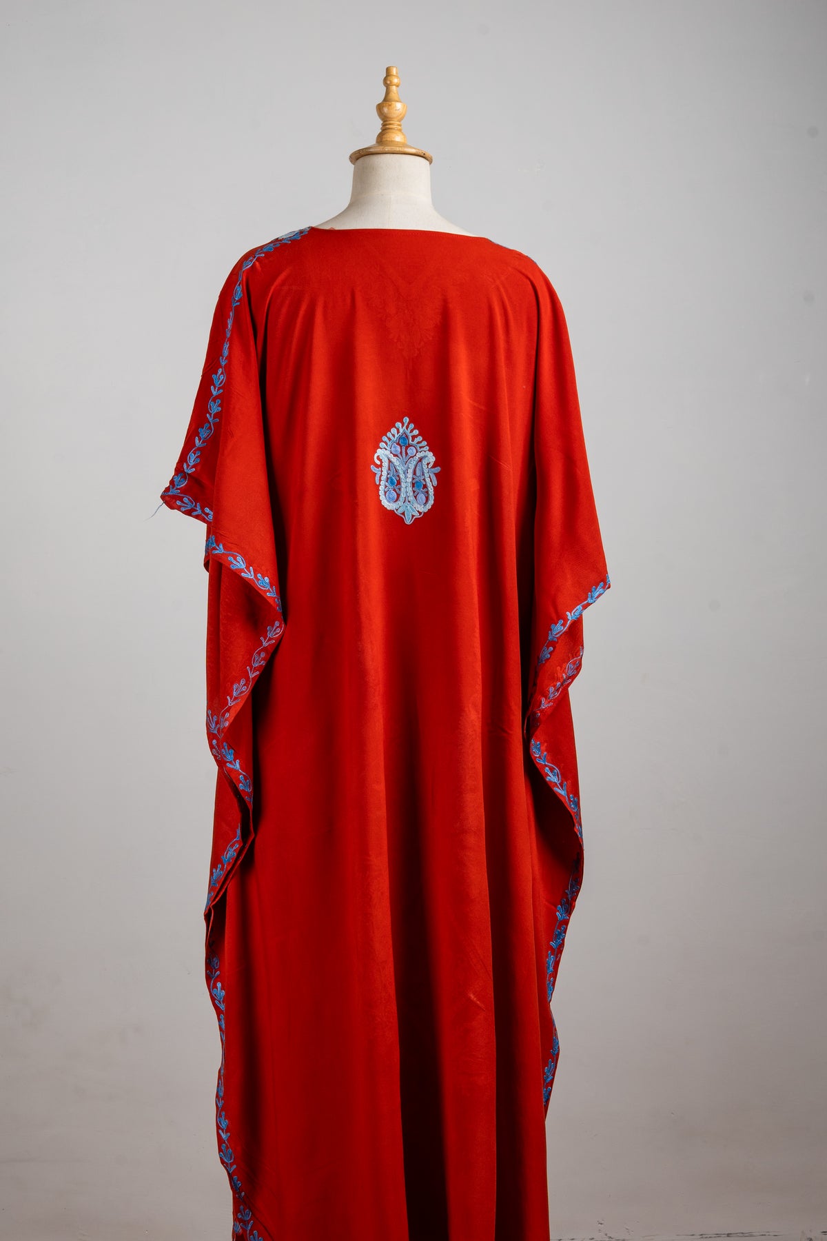 Full back view of the red kaftan with a small blue motif between the shoulders and blue-trimmed flowing sleeves.