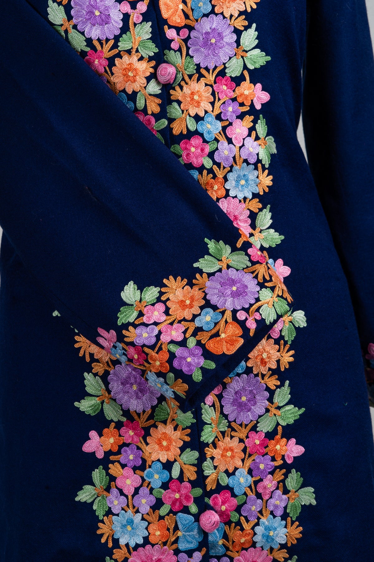 Detail of a navy jacket's crossed sleeve, with a multicoloured Aari floral cuff over dense flowers on the buttoned front
