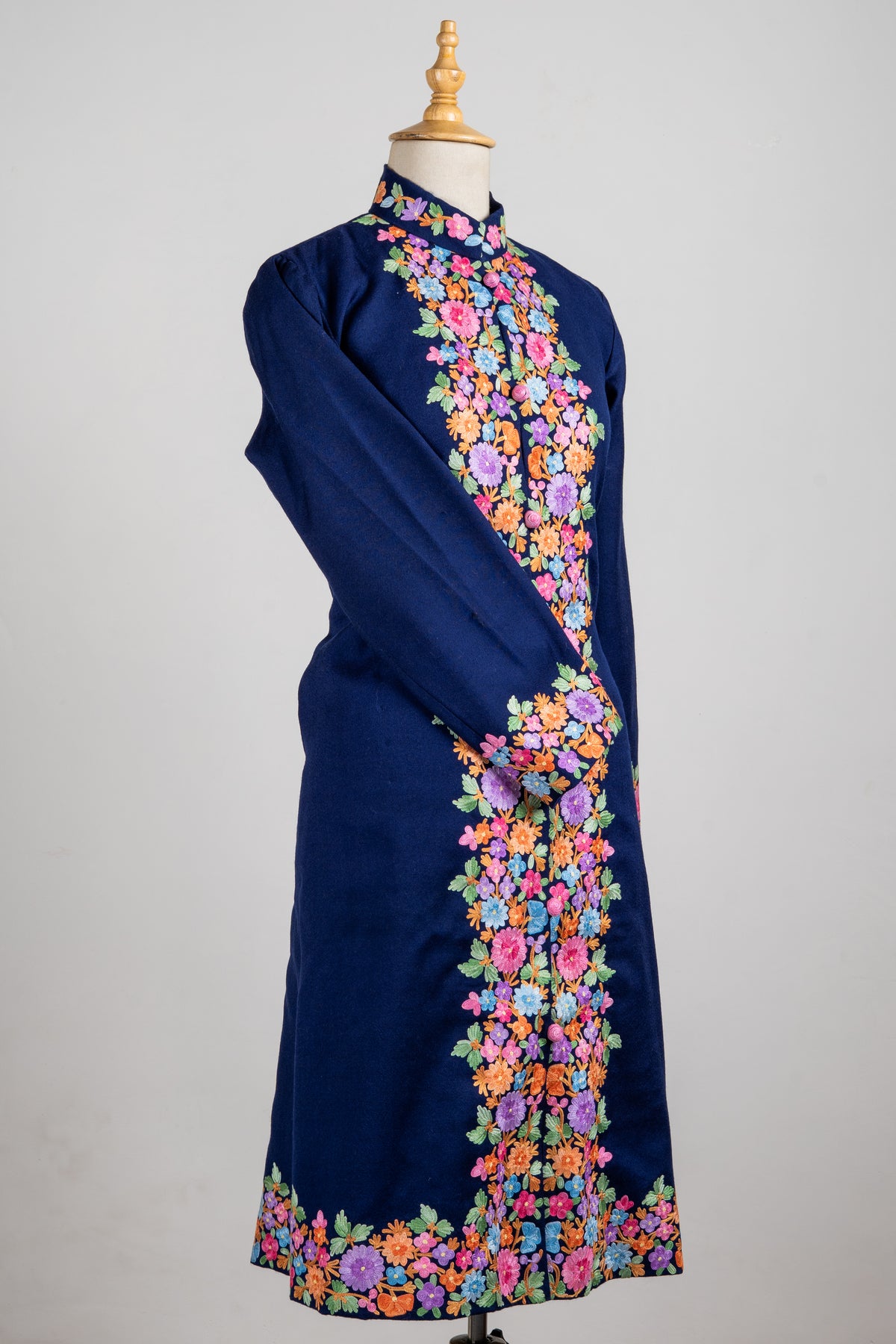 Angled navy long jacket on a mannequin with colourful Aari flower borders down the front, around the hem and across the cuff