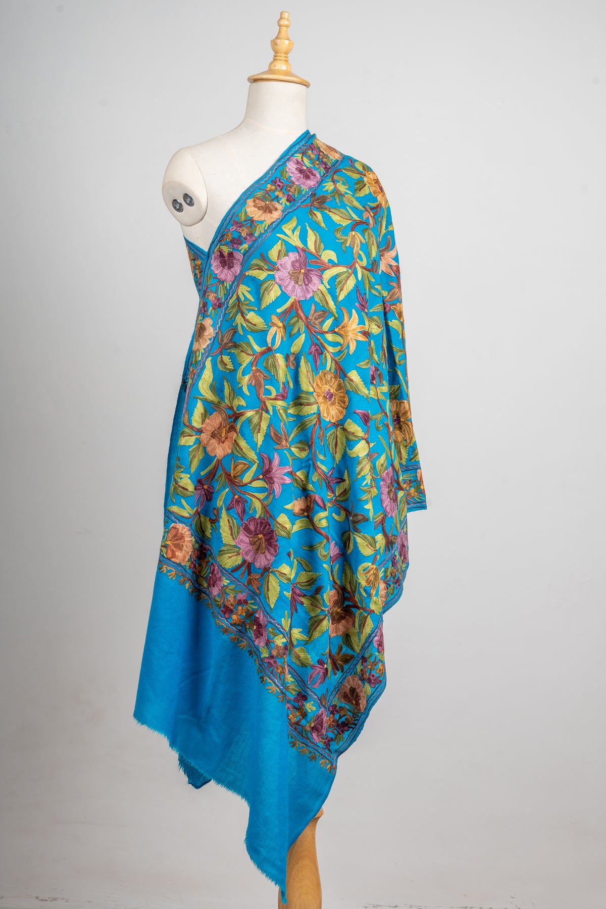 Angled view of the peacock-blue stole draped over a mannequin, showing the all-over floral embroidery and plain blue end