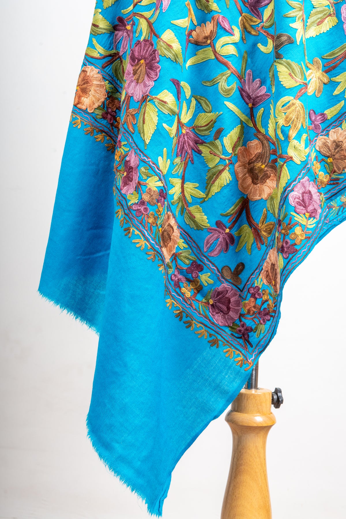Detail of the peacock-blue stole’s hanging corner, with colourful Aari flowers above a plain blue fringed end