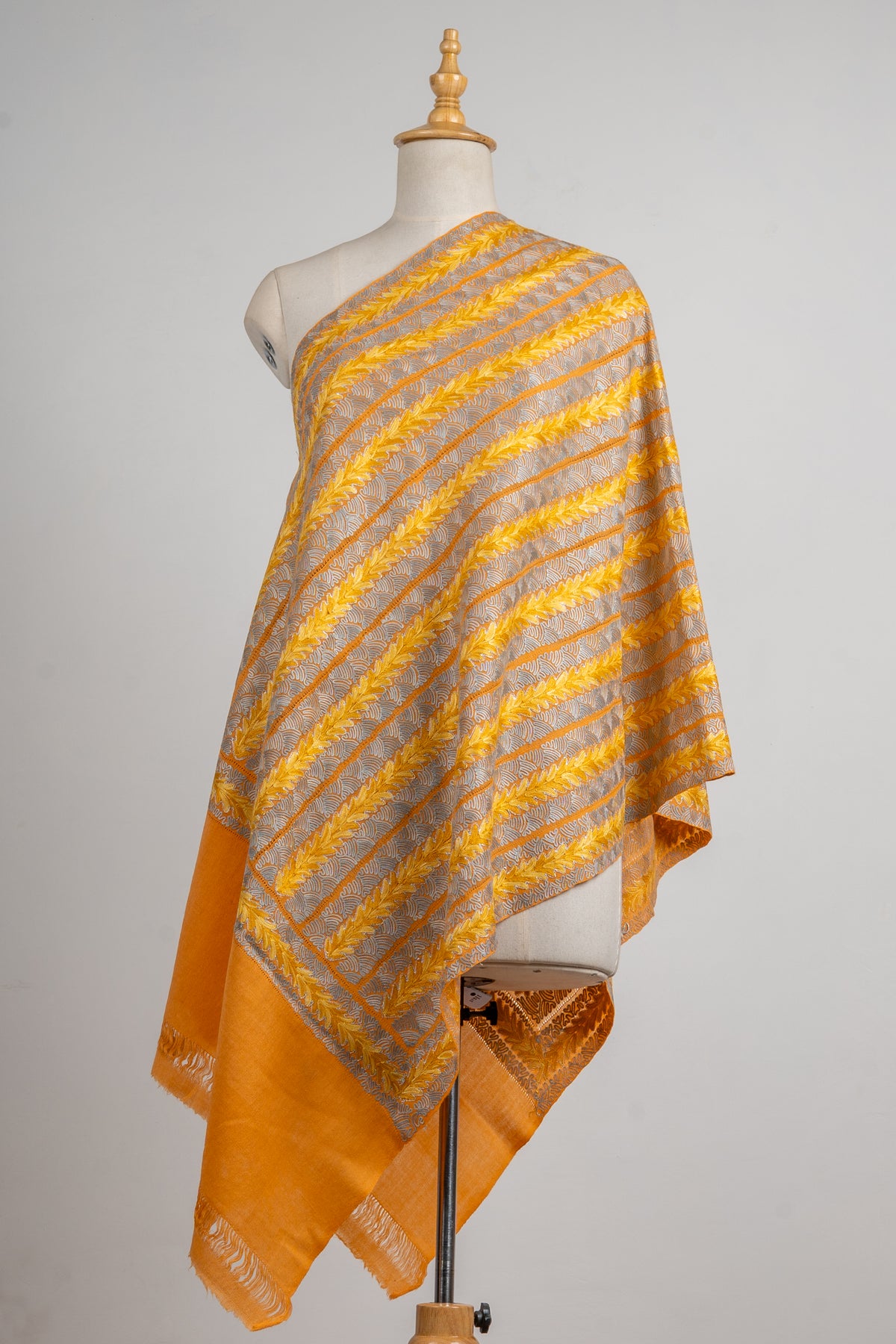 Golden stole draped on a mannequin with diagonal yellow leaf stripes, pale openwork bands and an orange fringed end