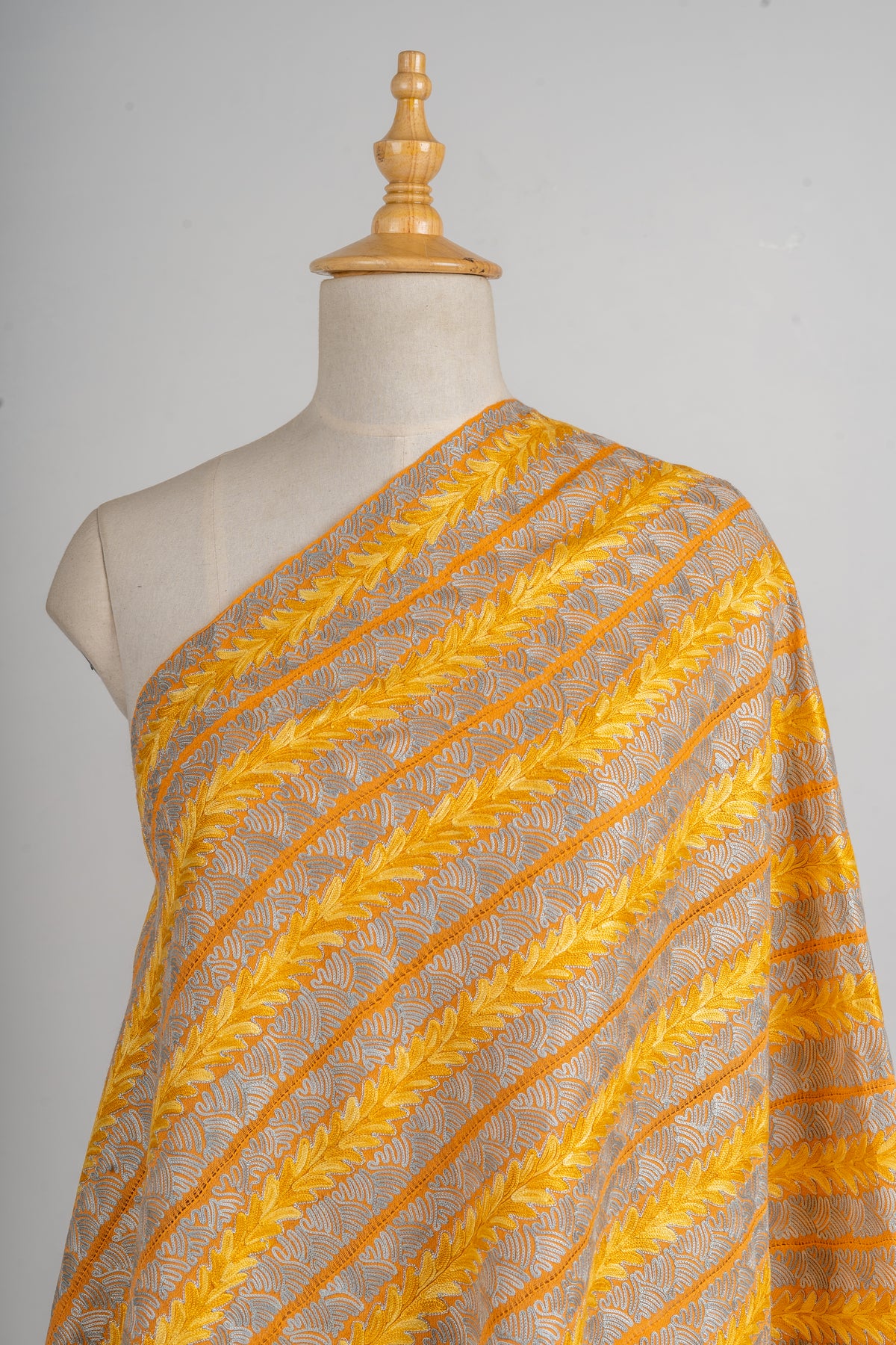 Golden Merino wool stole across a mannequin's shoulder, with yellow Aari leaf stripes alternating with pale openwork bands