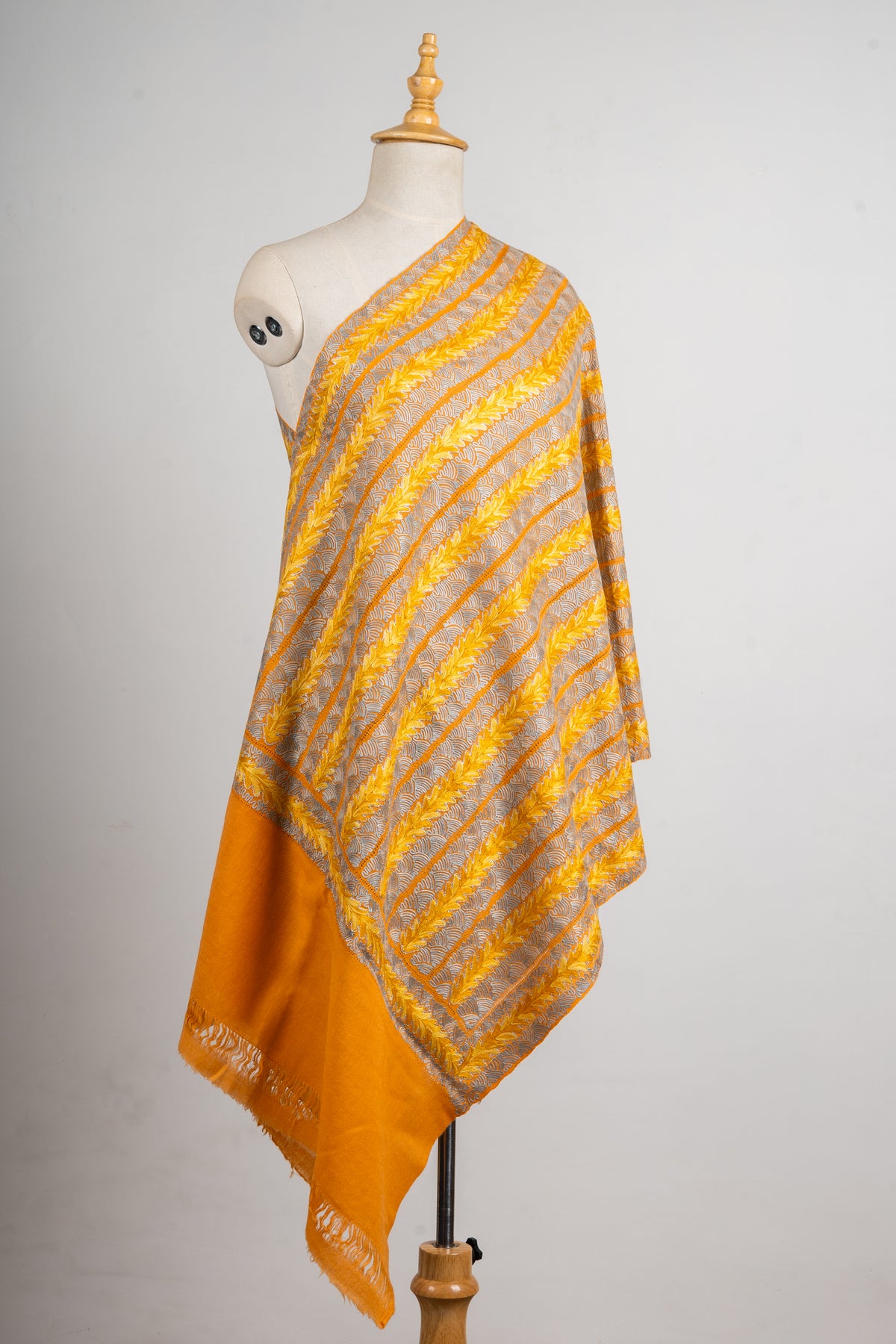 Full view of a golden Aari stole over one shoulder of a mannequin, showing striped cutwork and a long plain orange end