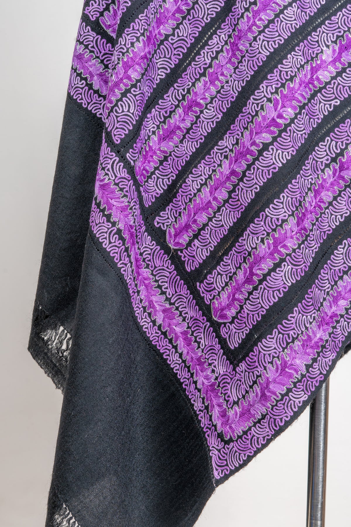 Hanging stole corner with purple floral stripes and lilac wavy edging above a plain charcoal fringed end.