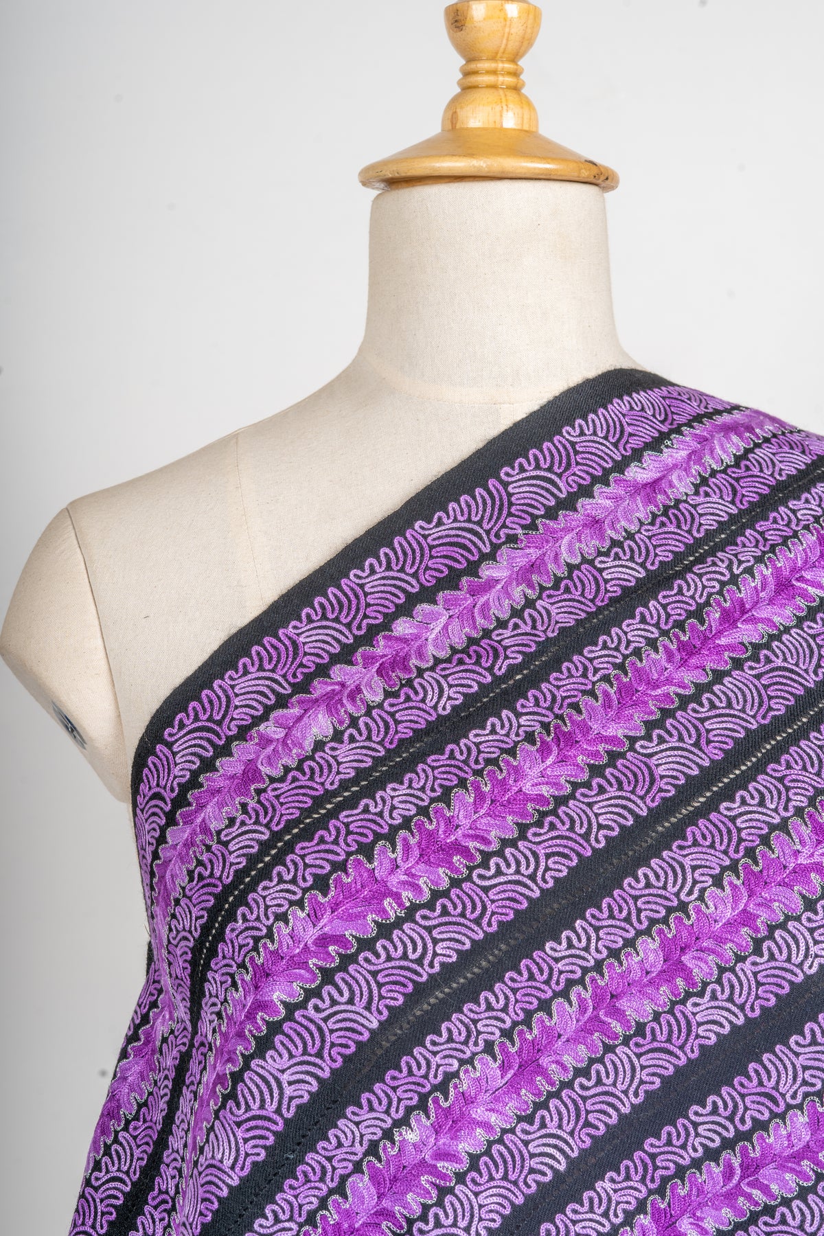 Shoulder close-up of the stole showing purple flower rows alternating with fine lilac wave patterns on charcoal fabric.