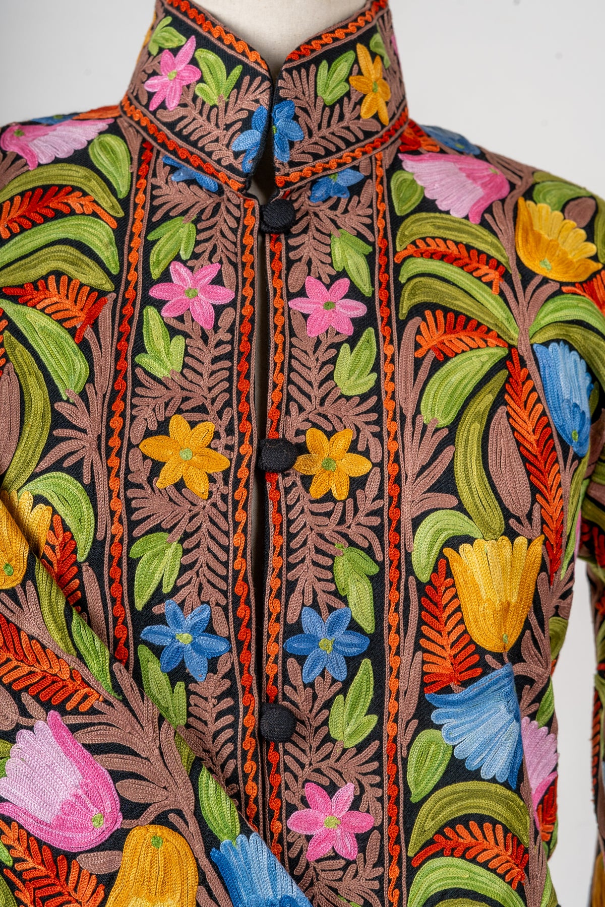 Close view of the jacket’s stand collar and black buttons, framed by pink, yellow and blue floral embroidery