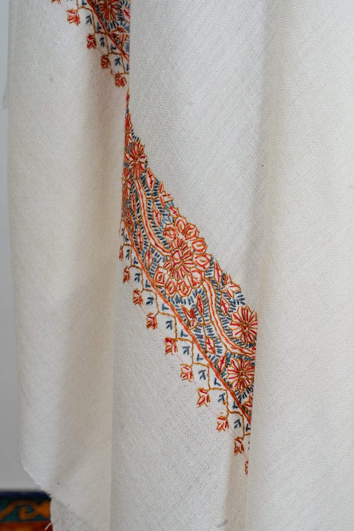 Draped close-up of the ivory shawl showing its orange floral border and small hanging motifs