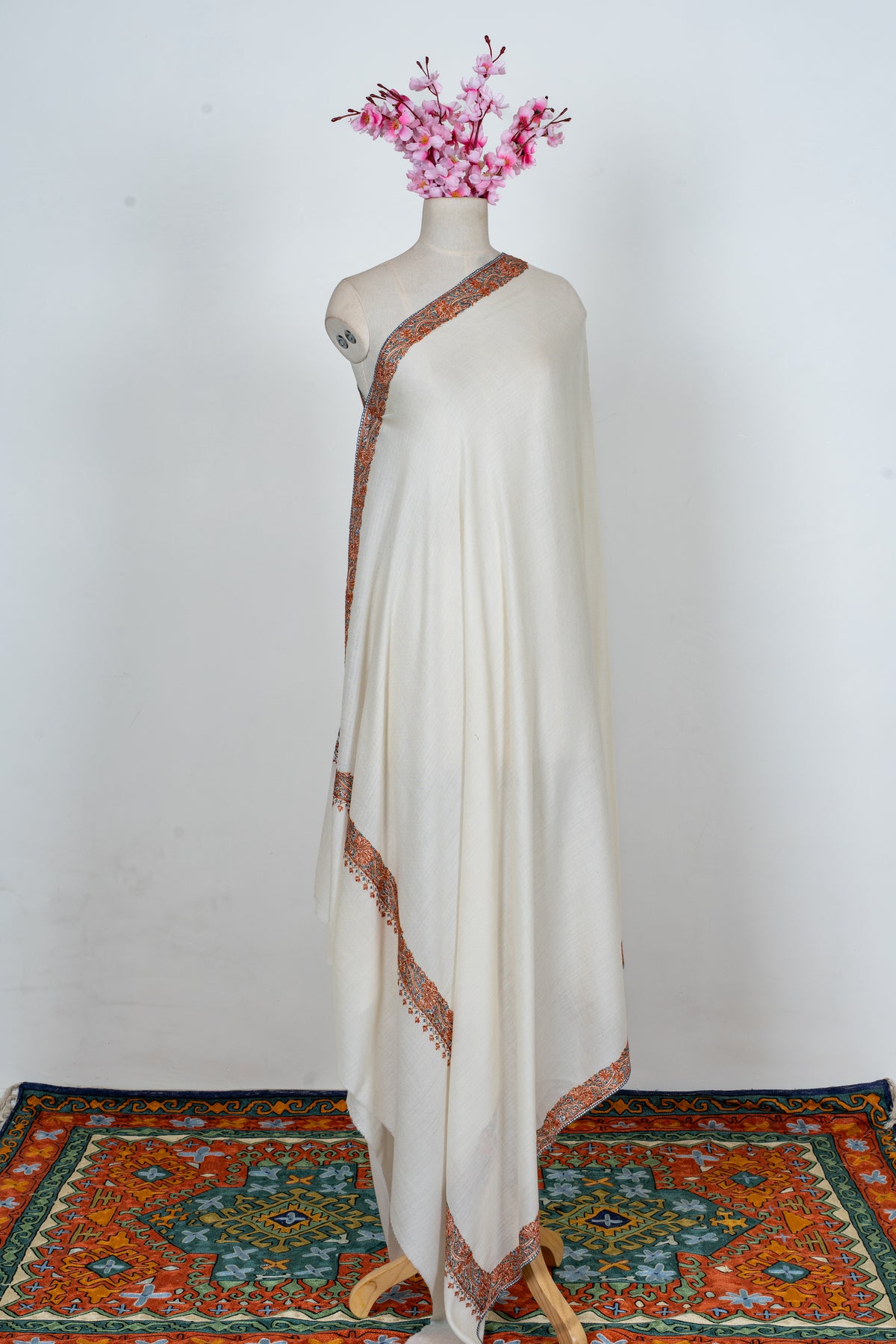 Full view of the ivory Merino wool shawl draped on a mannequin with narrow orange floral borders