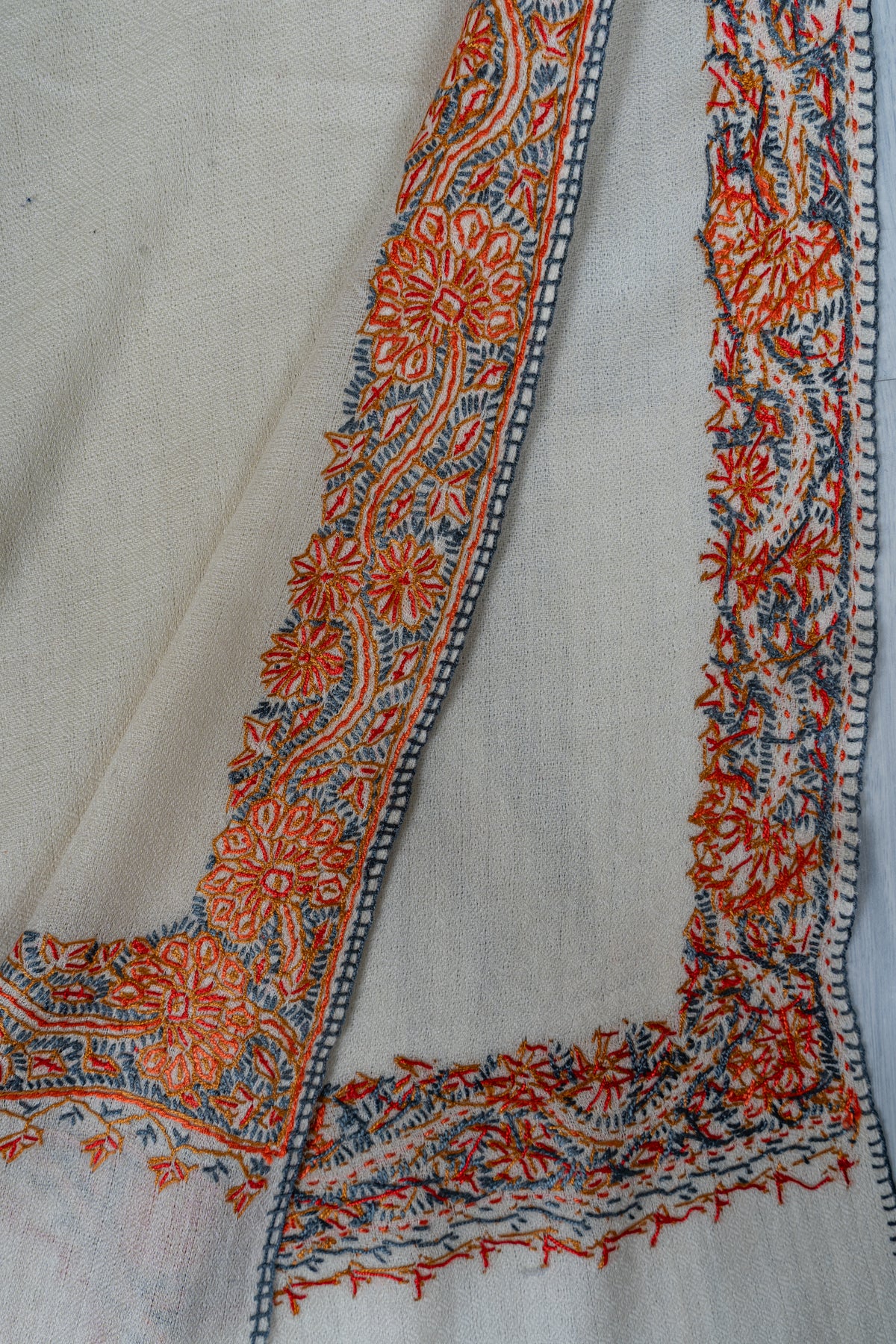 Folded ends of the ivory shawl showing orange and blue-grey embroidered borders on both sides