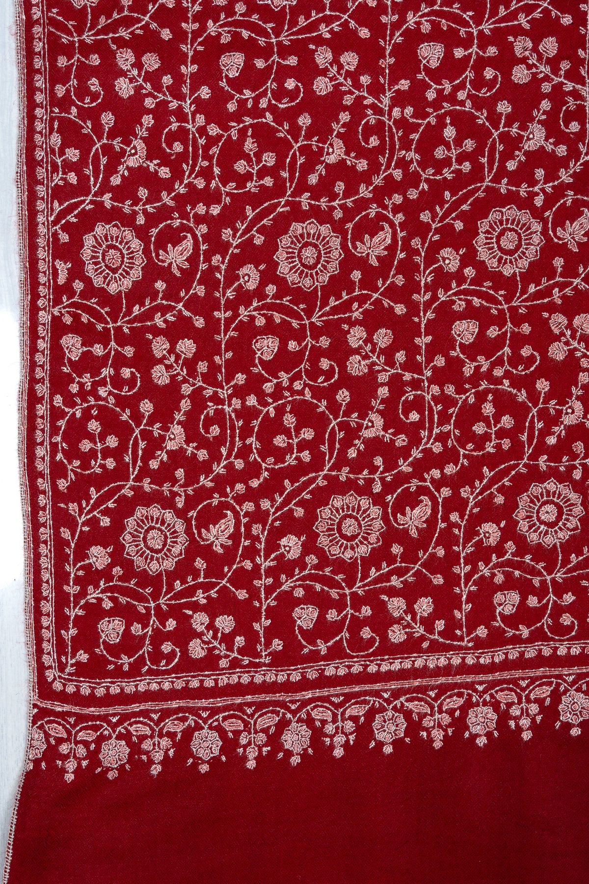 Corner detail of a crimson shawl with ivory Sozni flowers, curling vines and a delicate floral end border