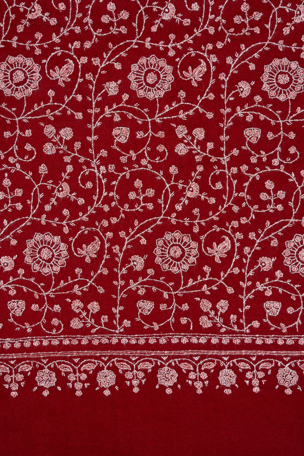 Close-up of round ivory Sozni flowers and curling vines above an ornamental border on crimson Pashmina