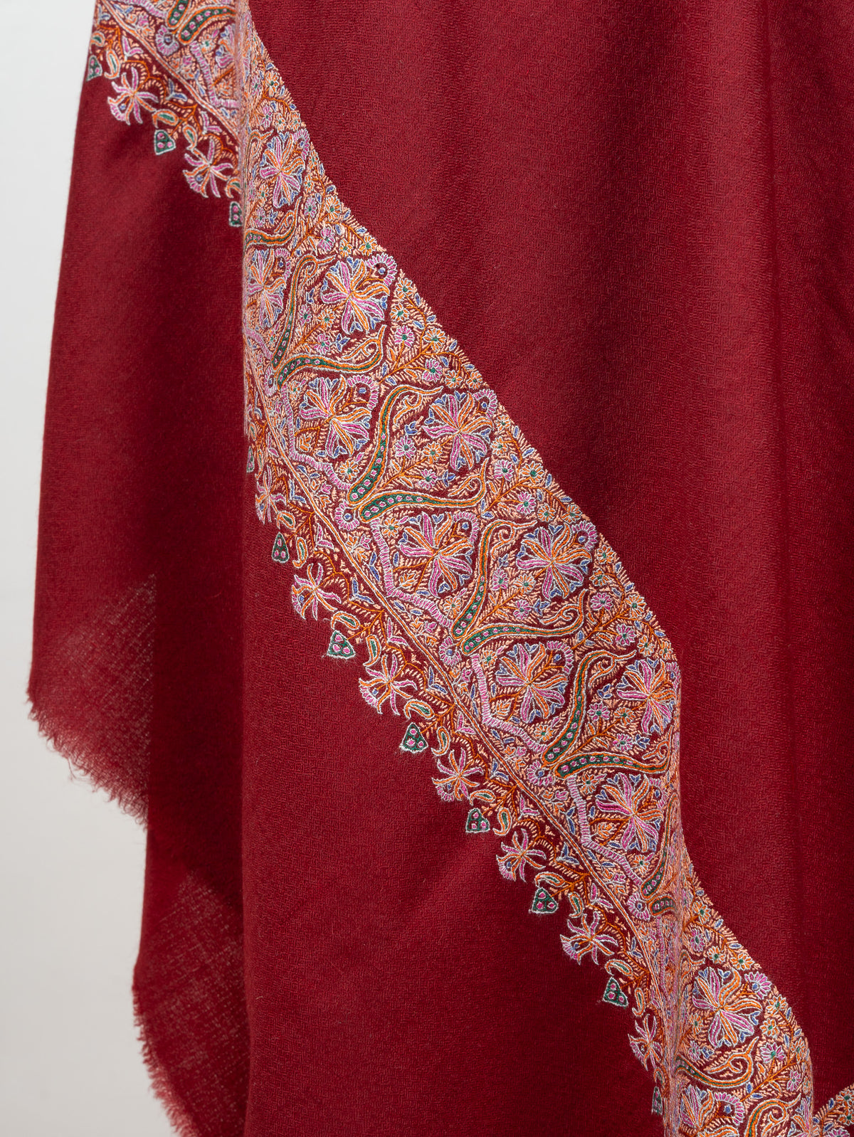 Draped crimson shawl folds showing a pastel floral border with small hanging motifs