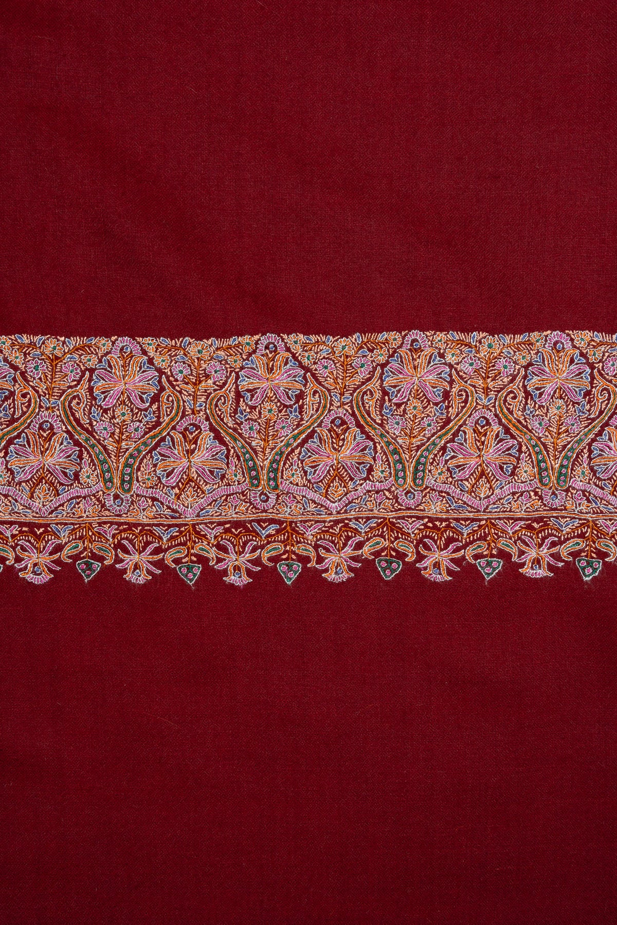 Close-up of pastel Sozni flowers and small hanging motifs across the crimson shawl's end border