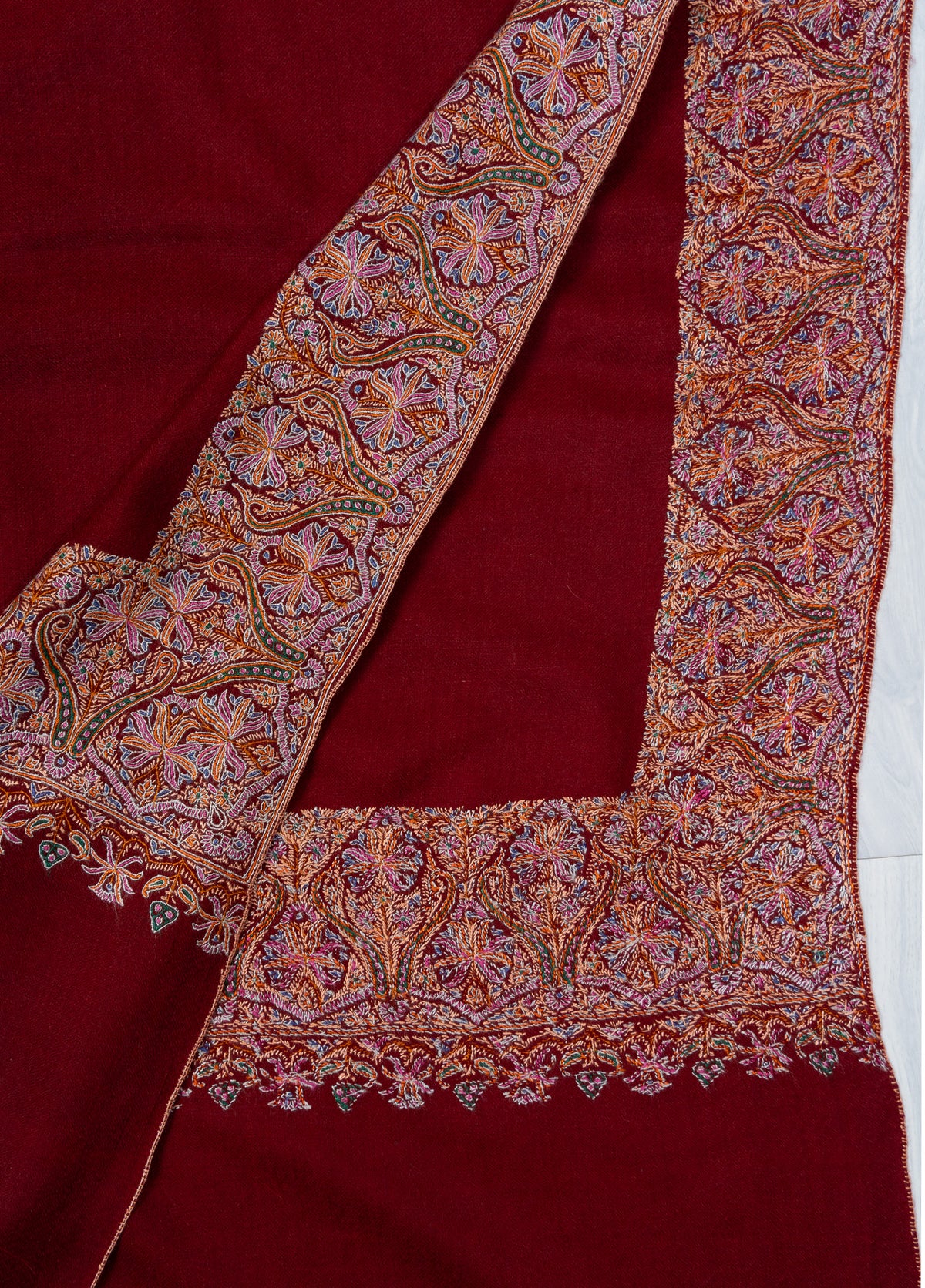 Folded crimson shawl corners showing the front and reverse of multicoloured Sozni border stitching