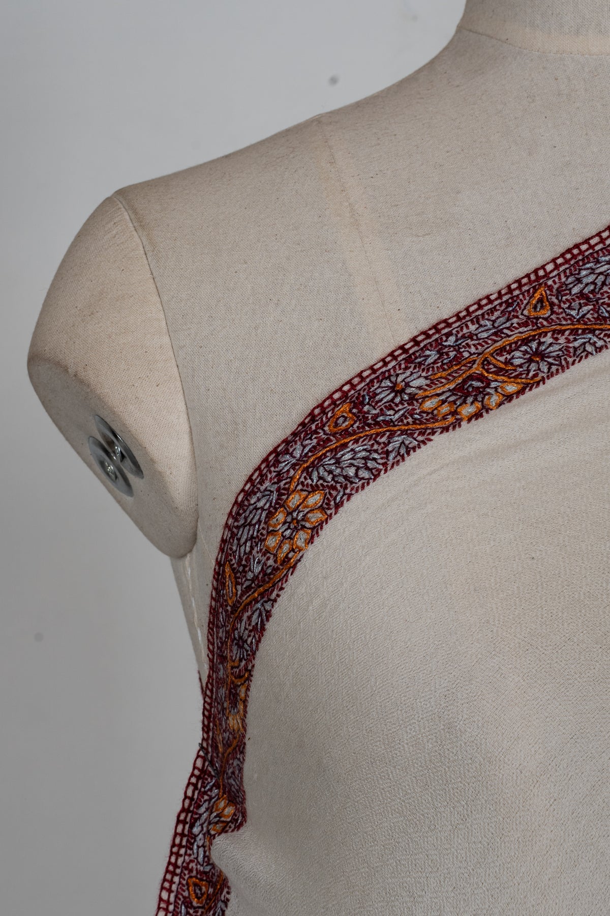 Shoulder close-up of the ivory shawl's burgundy and orange hand-embroidered floral border