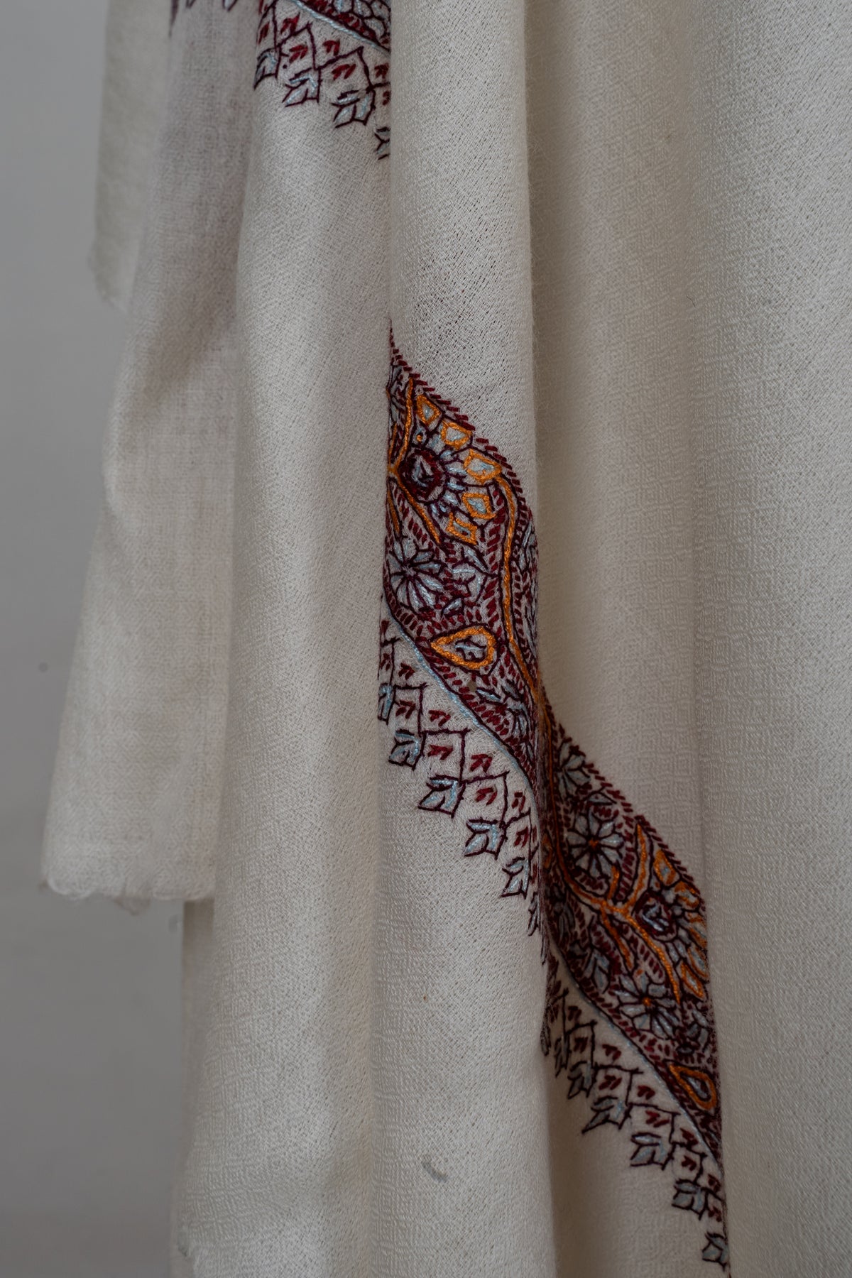 Draped detail of the ivory shawl showing its floral border and small burgundy hanging leaf motifs