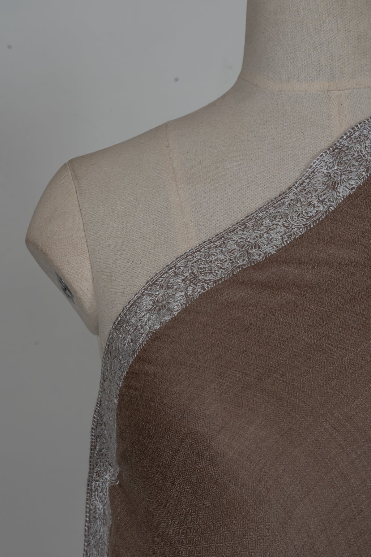 Close-up of the silver floral embroidered border along the edge of a walnut-brown Merino wool shawl