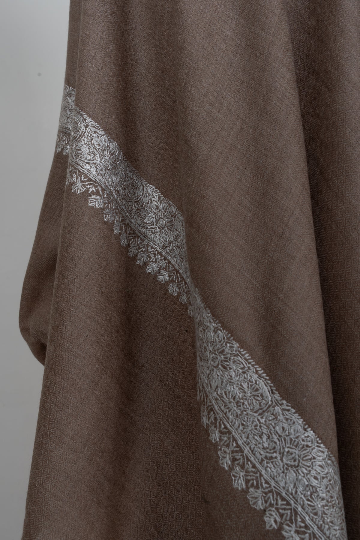 Hanging end of a walnut-brown Merino wool shawl with silver floral embroidery and small leaf motifs along the border
