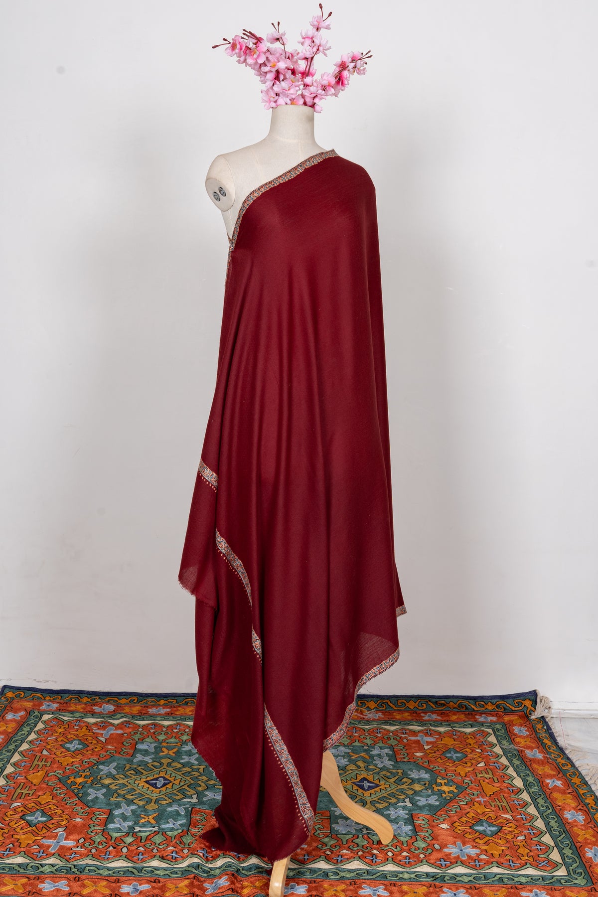 Full view of the maroon Merino wool shawl draped on a mannequin with narrow embroidered borders