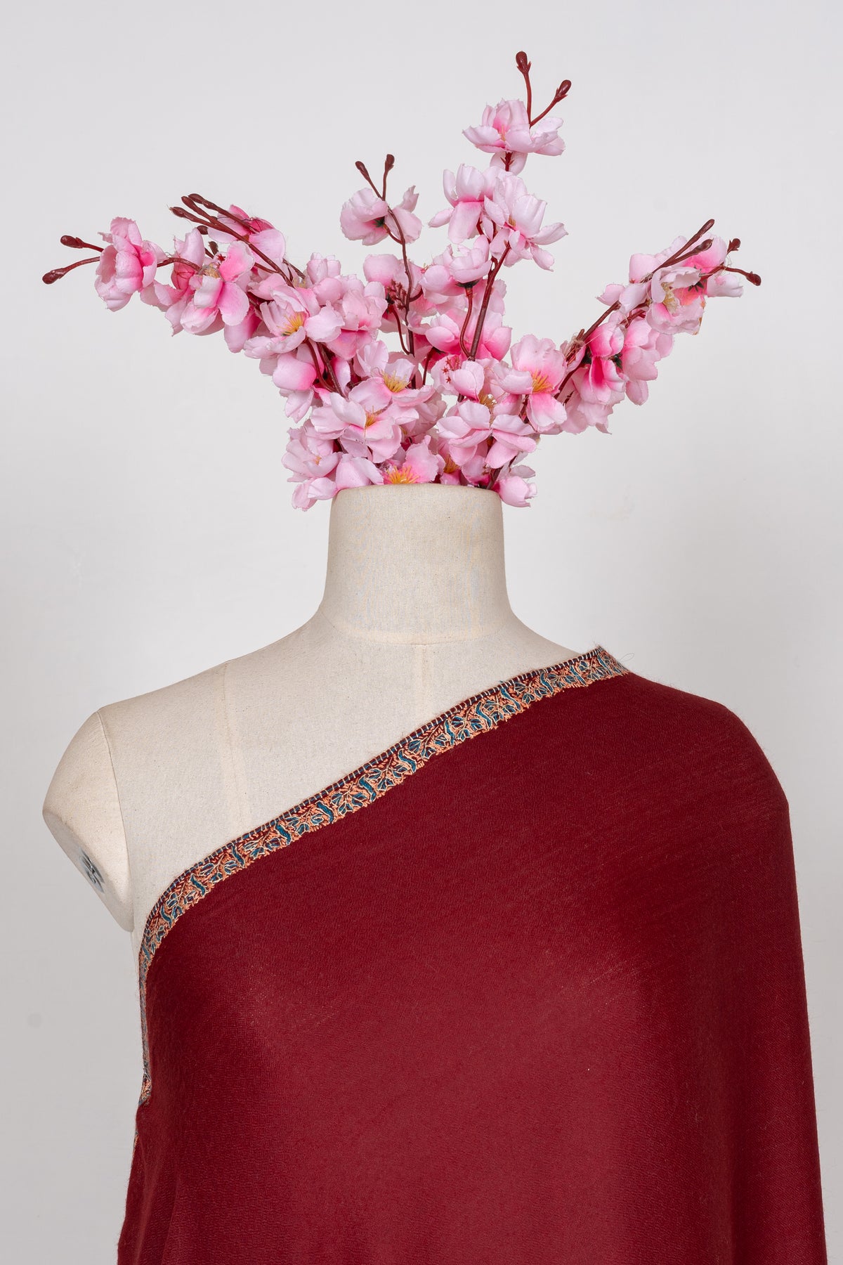 Upper view of the maroon shawl on a mannequin, showing its plain field and narrow teal and beige border