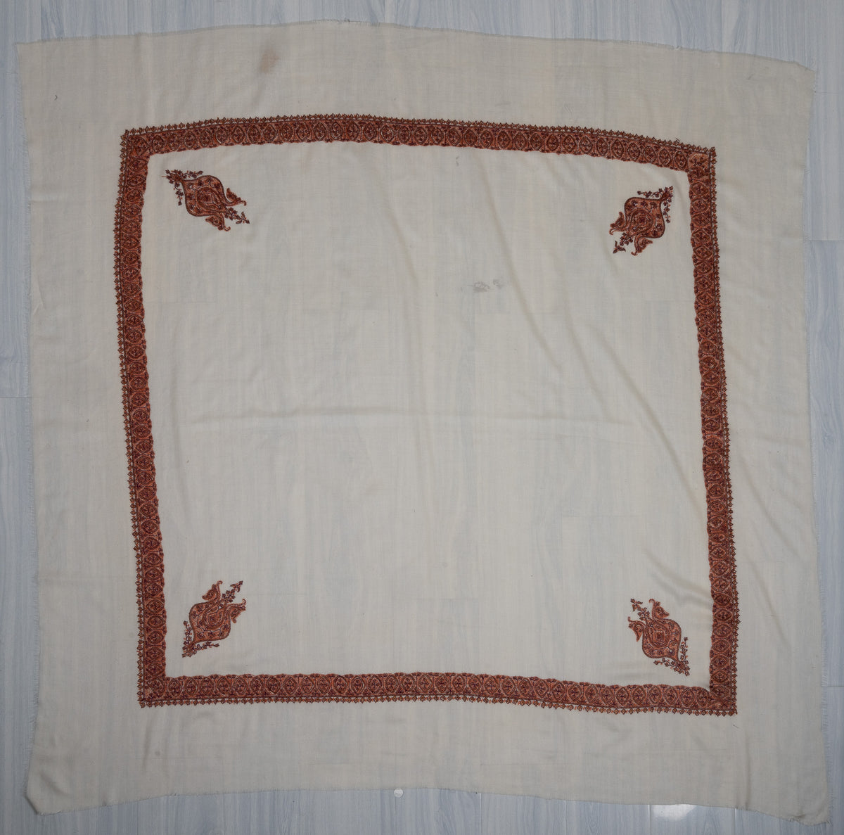 Square ivory rumal laid flat with four cinnamon-toned Sozni corner motifs, a narrow floral border and a plain centre